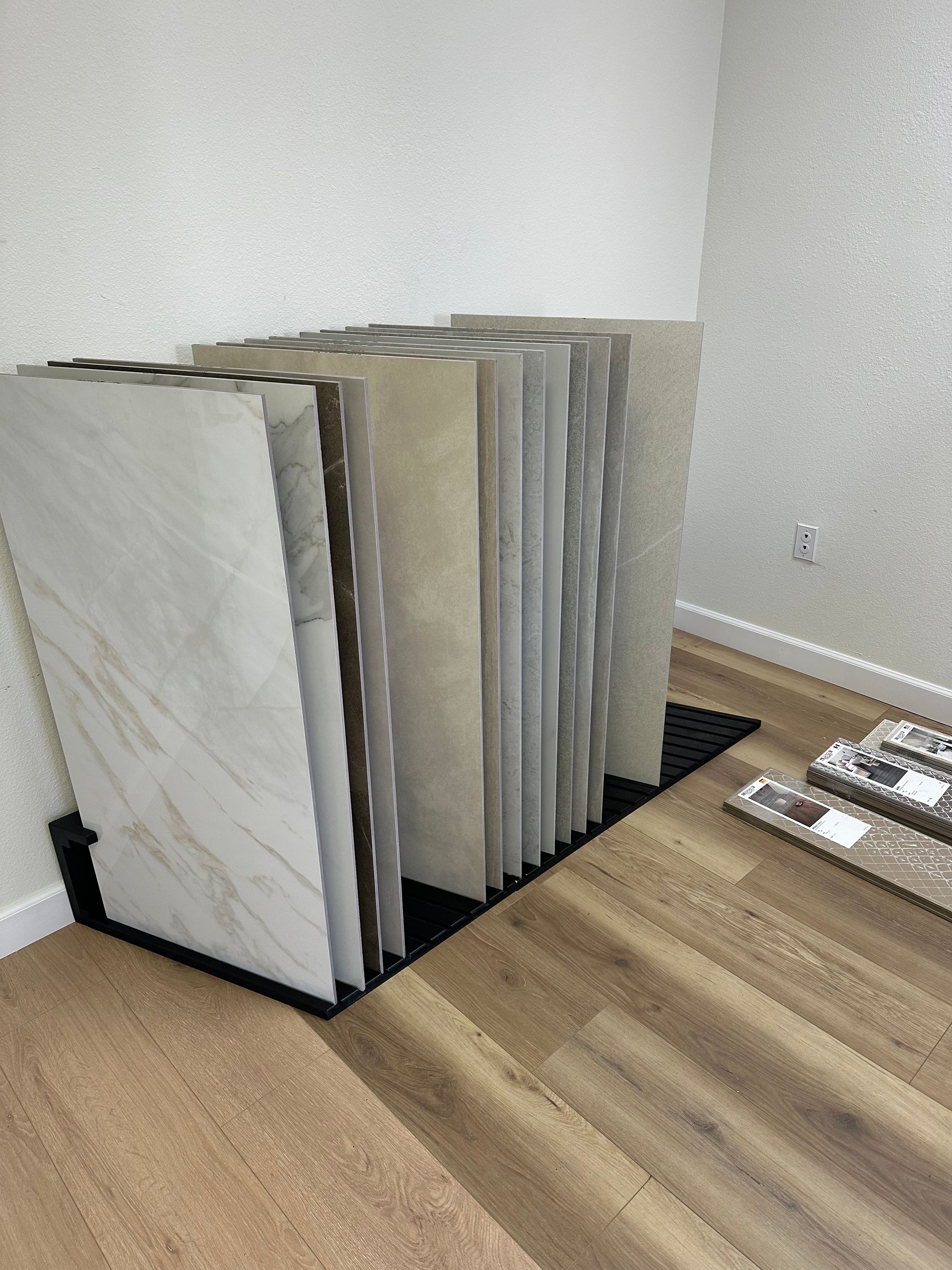 Tile samples displayed on a rack against a white wall in a showroom. Wooden floor in the foreground.
