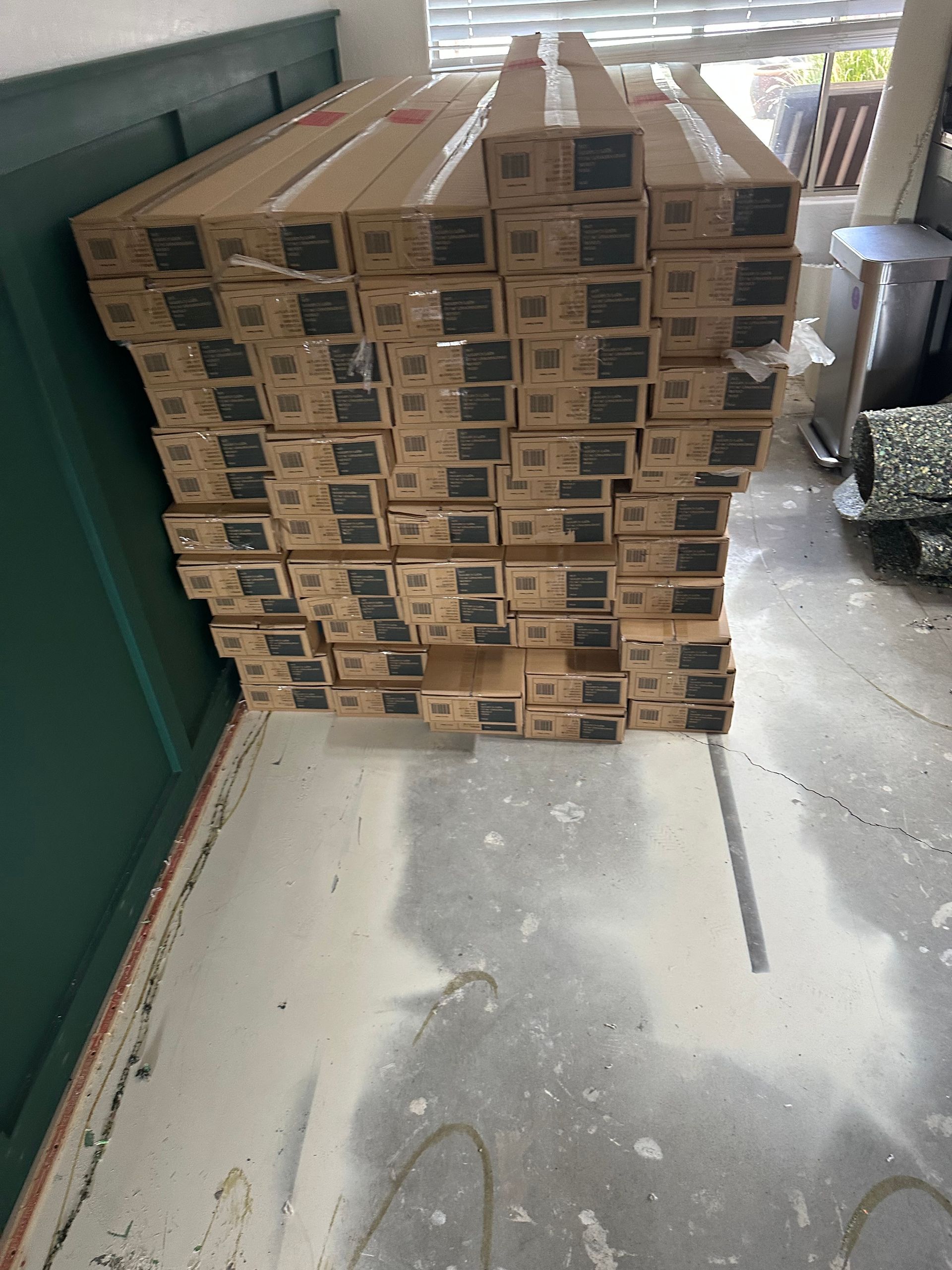 Stack of brown boxes in a concrete floored room. Boxes lean against a green wall.