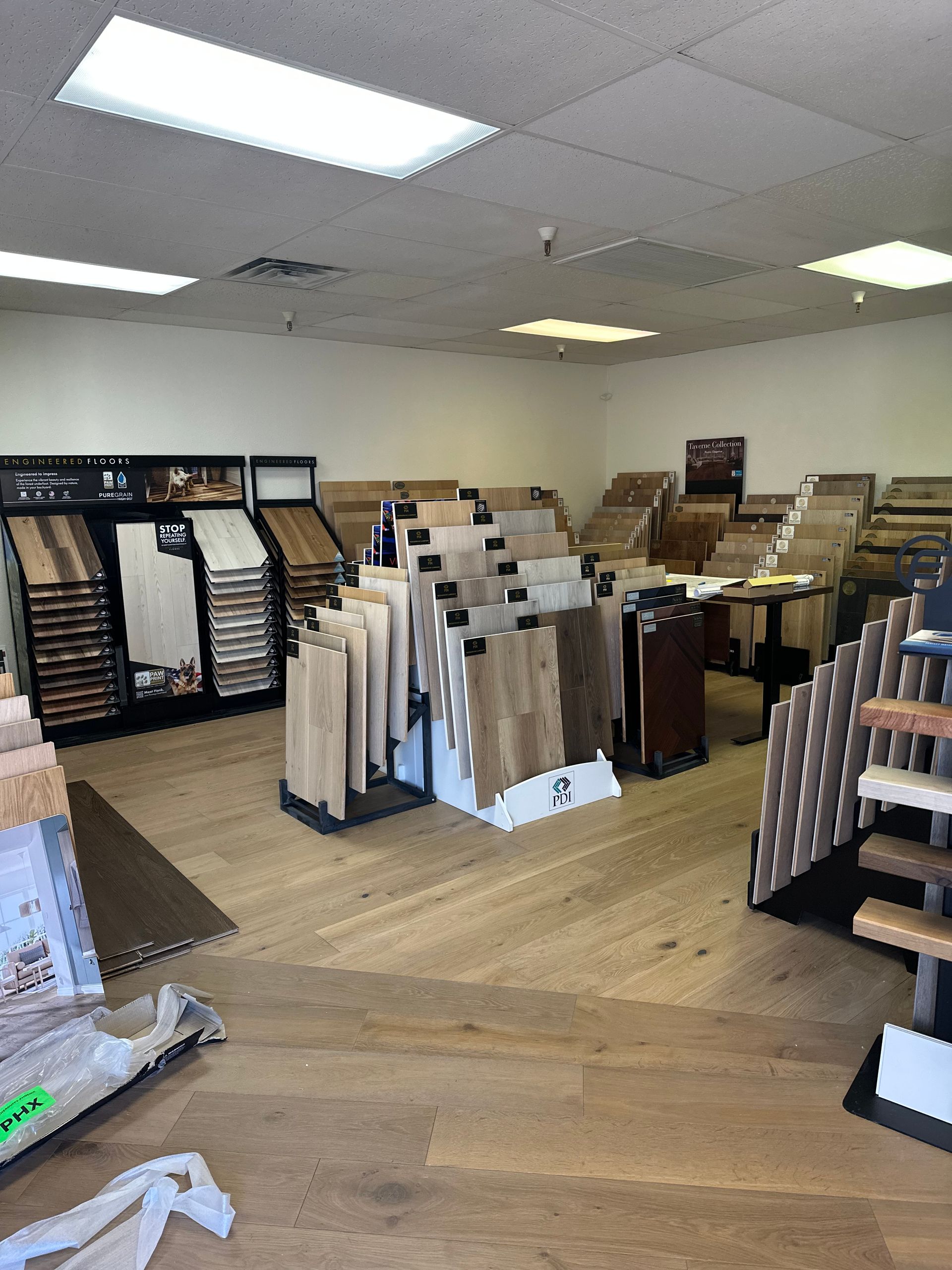 Flooring showroom with various samples on display. Light wood flooring, bright overhead lights.