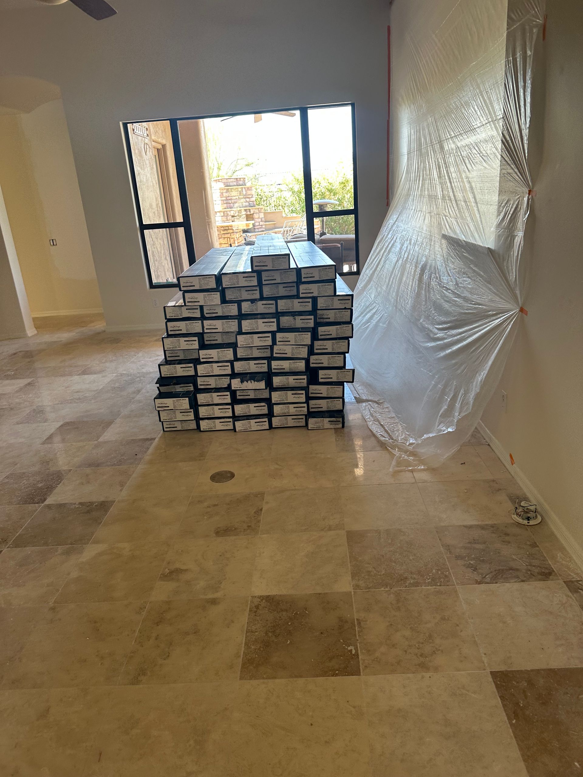 Stack of flooring boxes on a tiled floor in a room with a window.