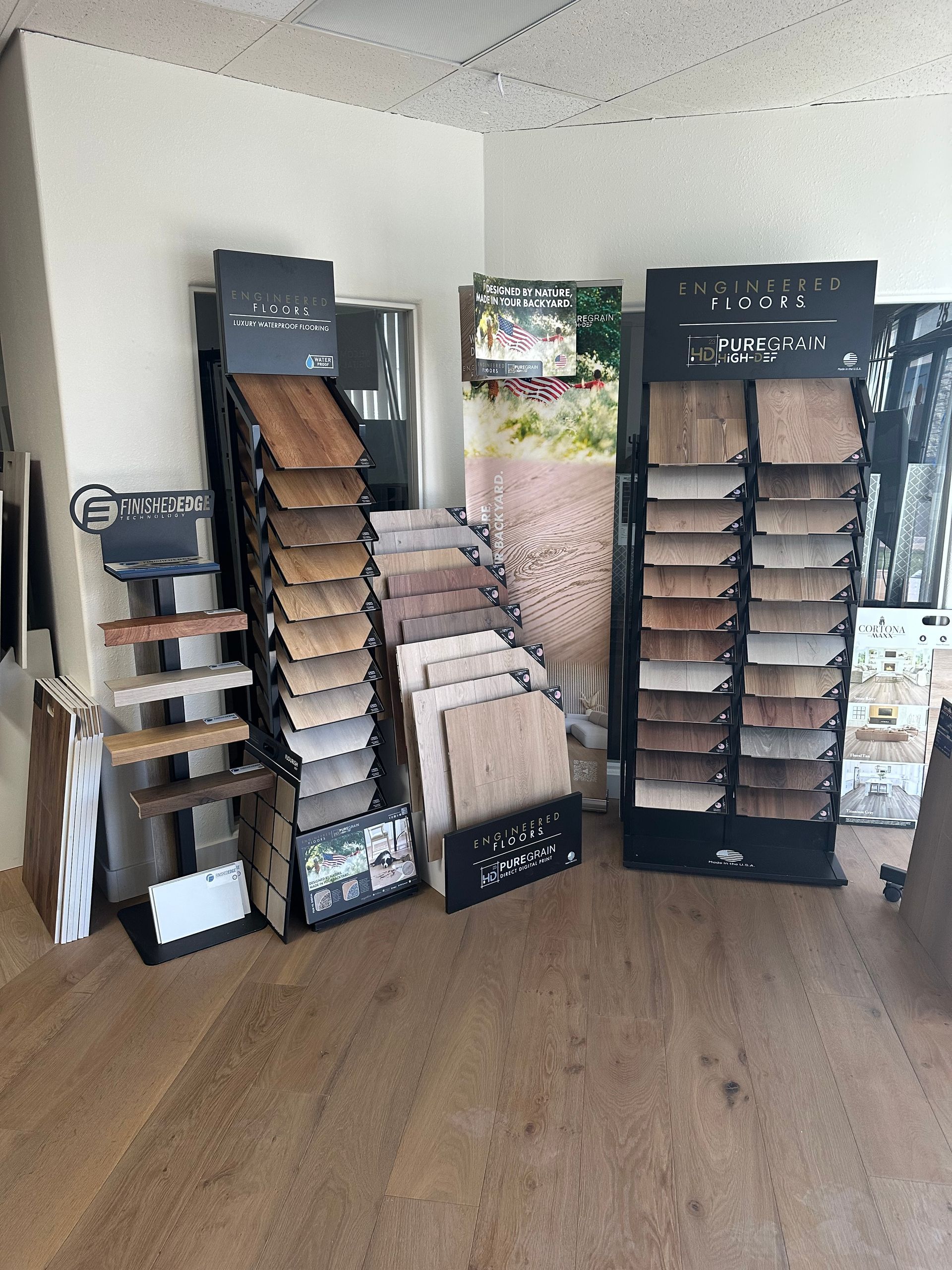 Displays of flooring samples in a store: various wood tones, light tile, against a wooden floor.