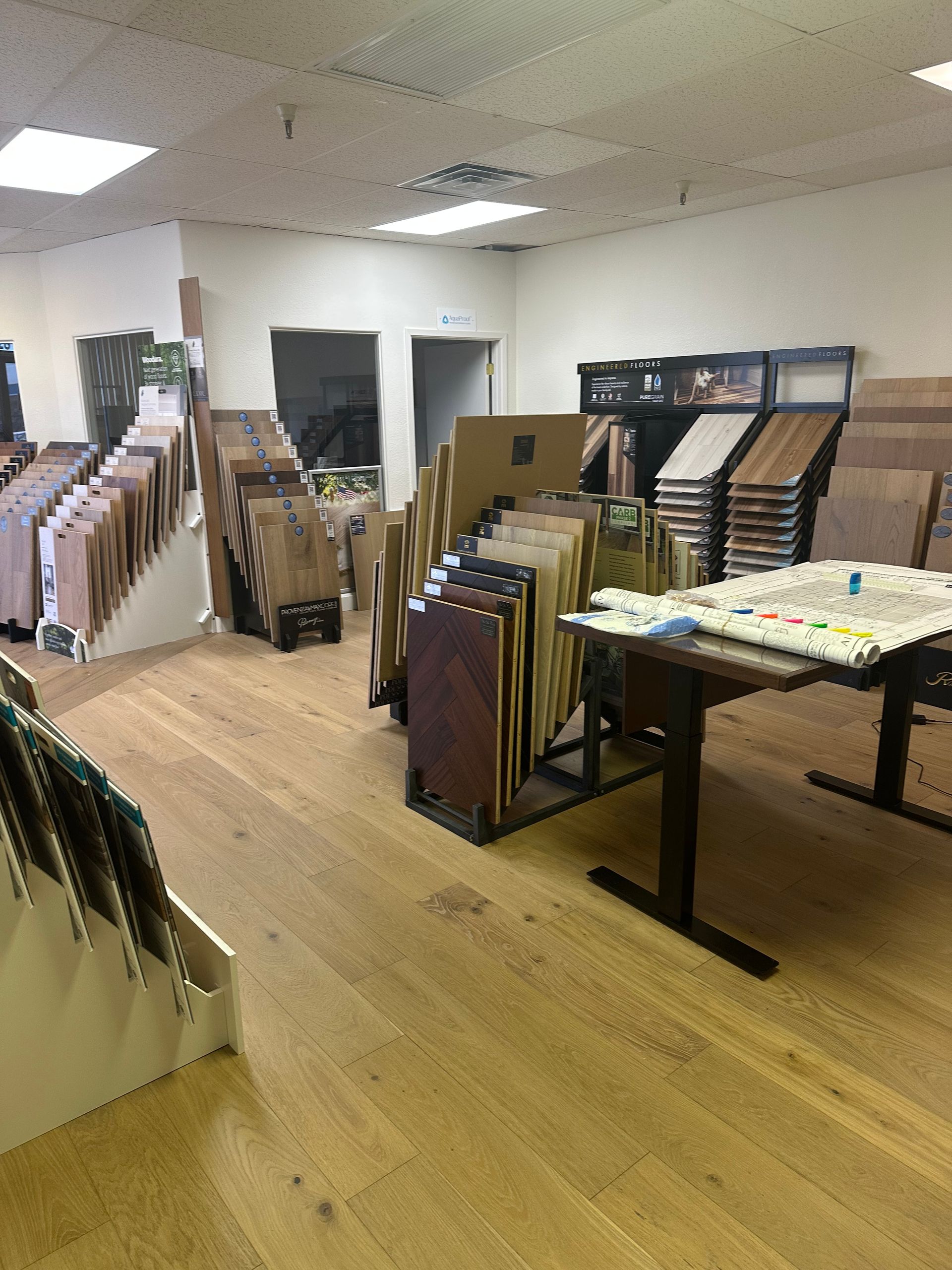 Flooring samples displayed in a showroom. Light wood floors, many wood samples are in racks and on the table.