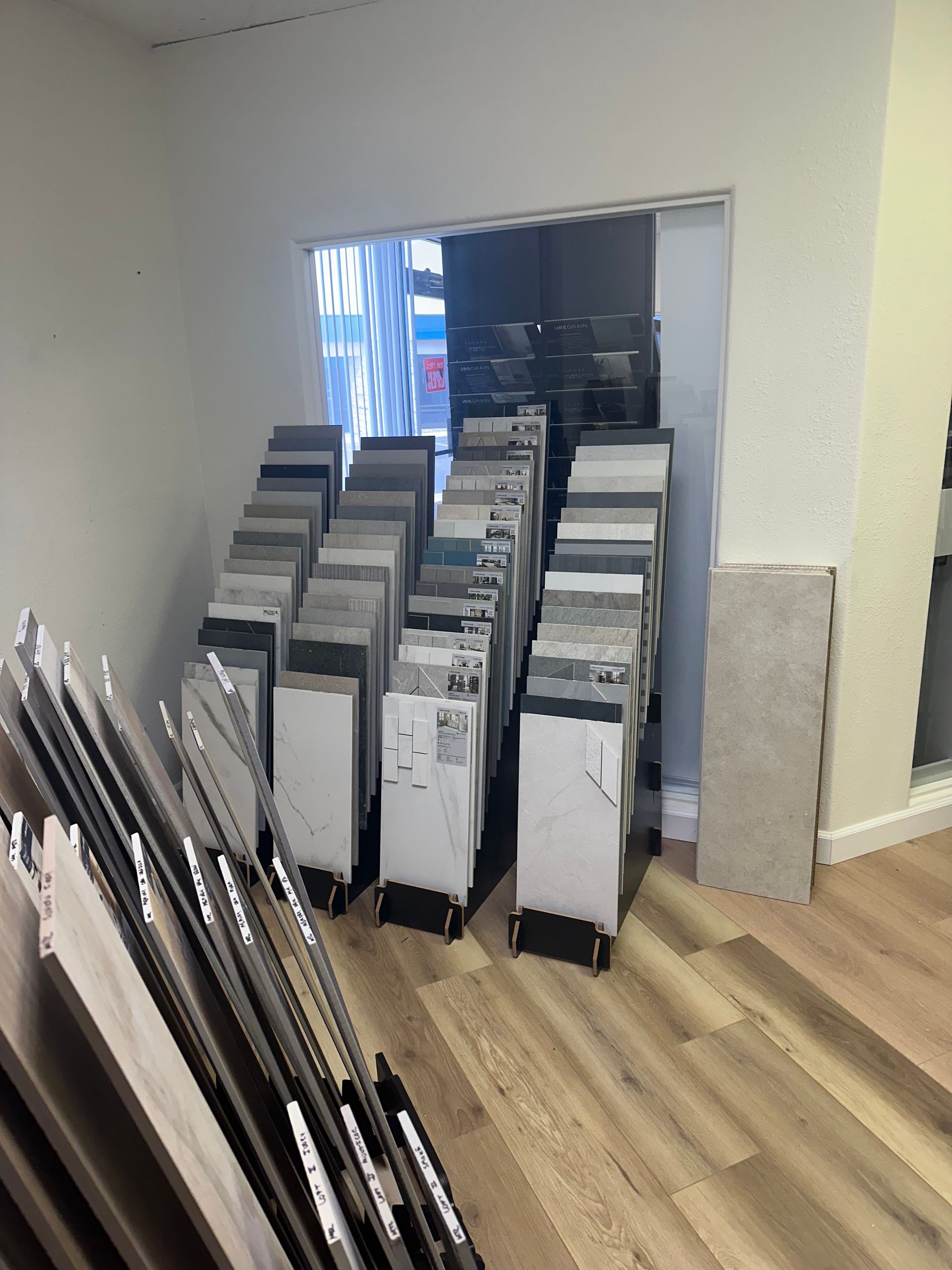 A showroom displaying various flooring samples arranged against a white wall and doorway. Wooden floor in foreground.