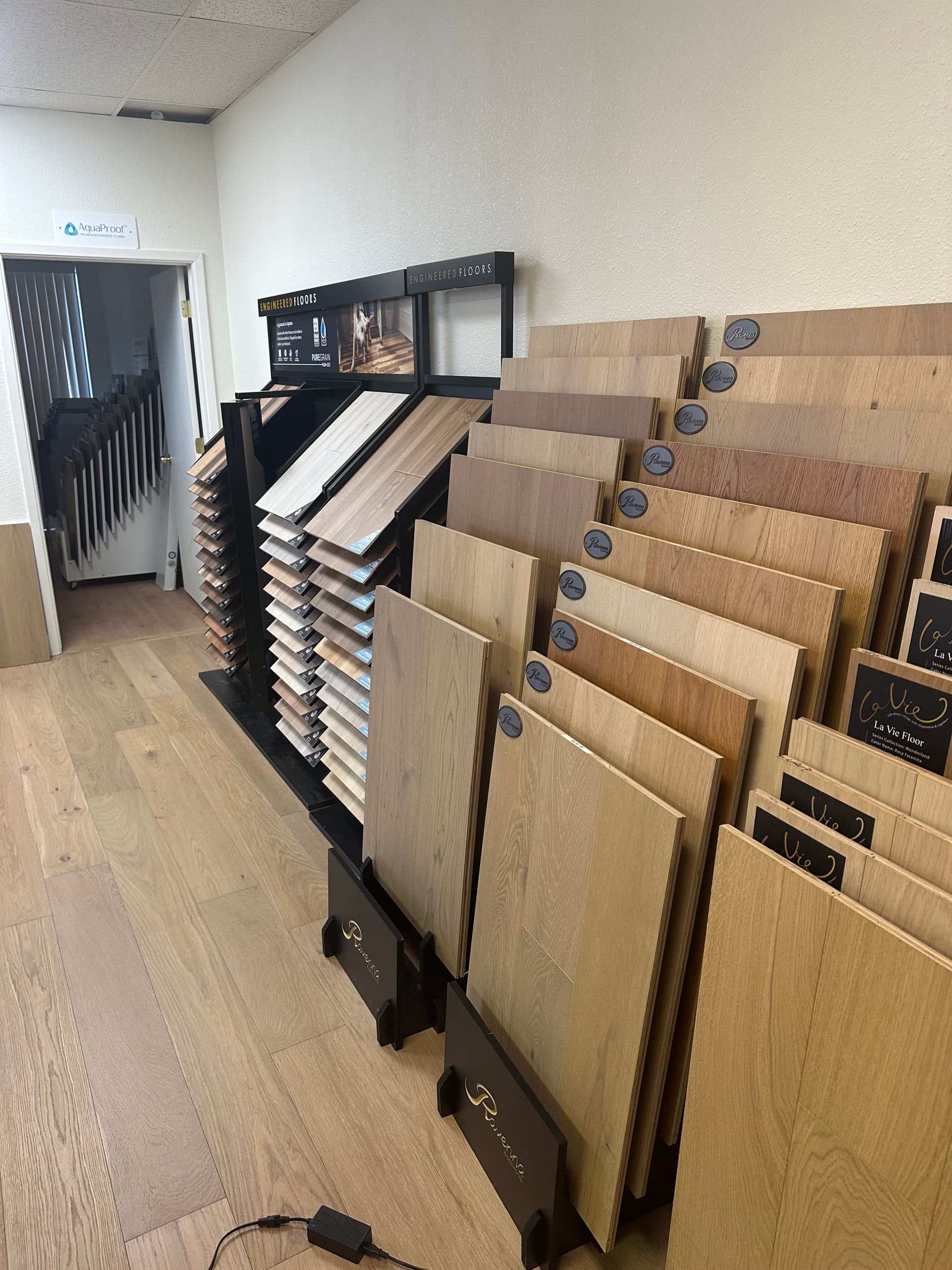Flooring samples on display in a store. Various wood tones and textures. Doorway to stairs in background.