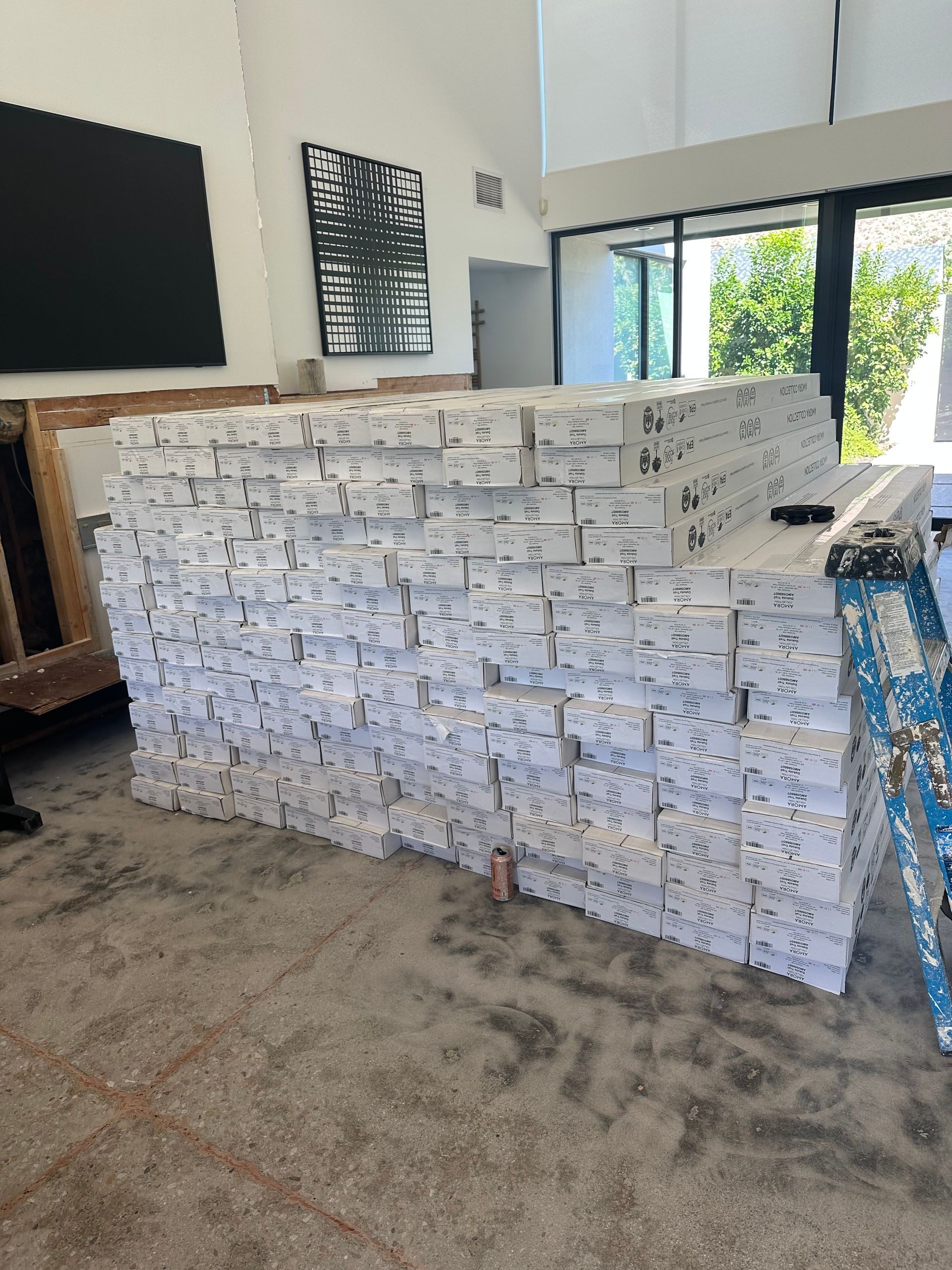 Large stack of white boxes inside a building, next to a ladder and a window.