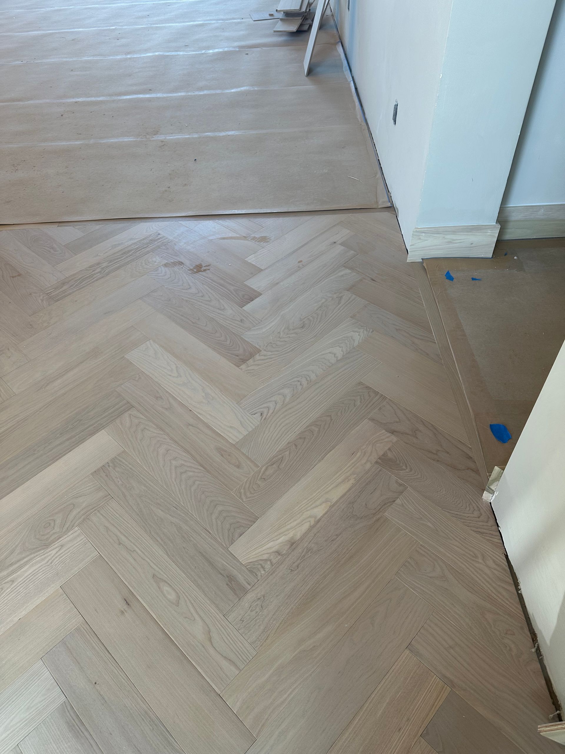 Herringbone wood floor installation, light-colored wood.