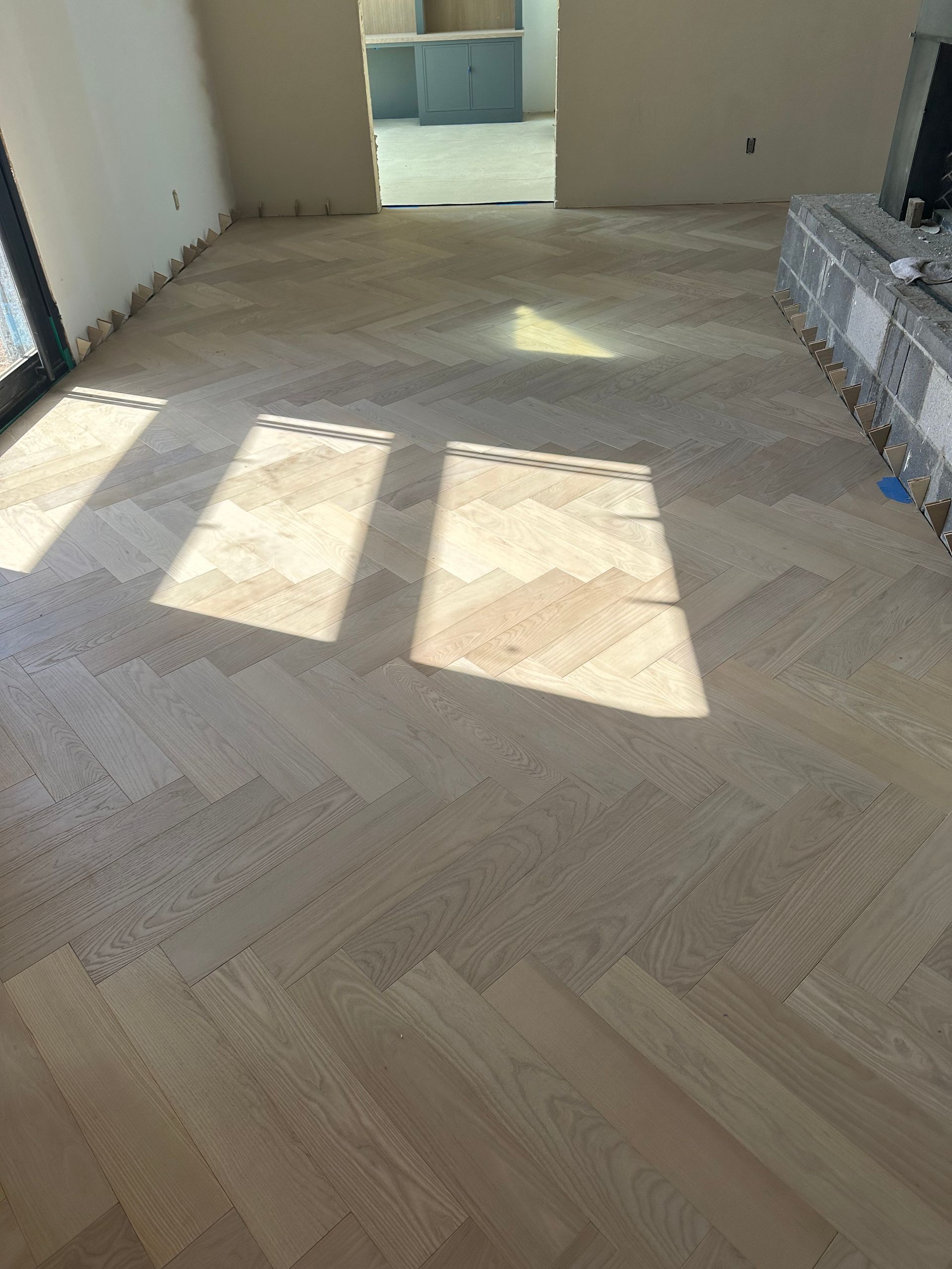 Herringbone wood flooring in a room, sunlight streaming through windows.