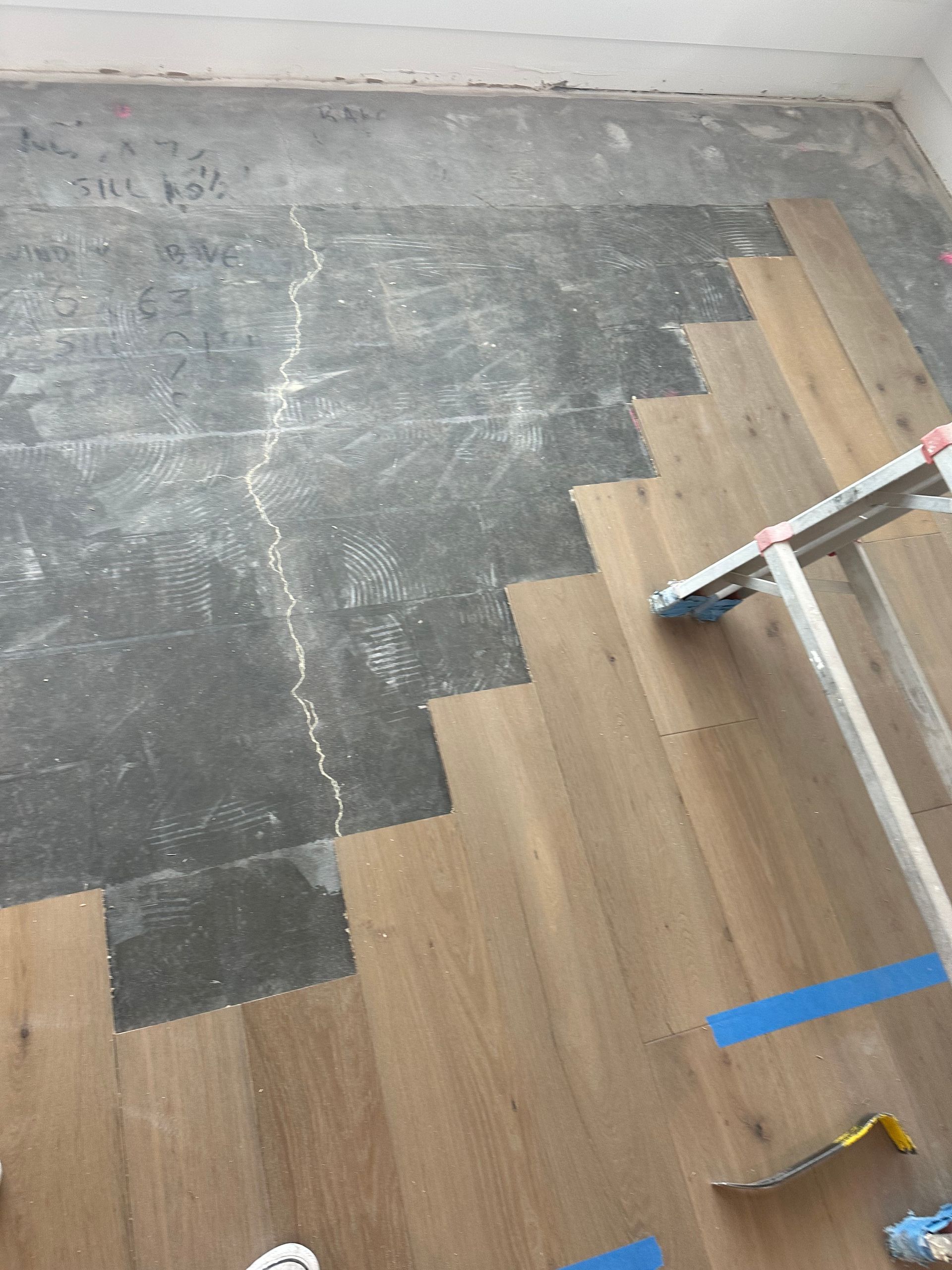 Wooden floor installation in progress. Light brown wood planks laid on concrete floor, with a section still uncovered.