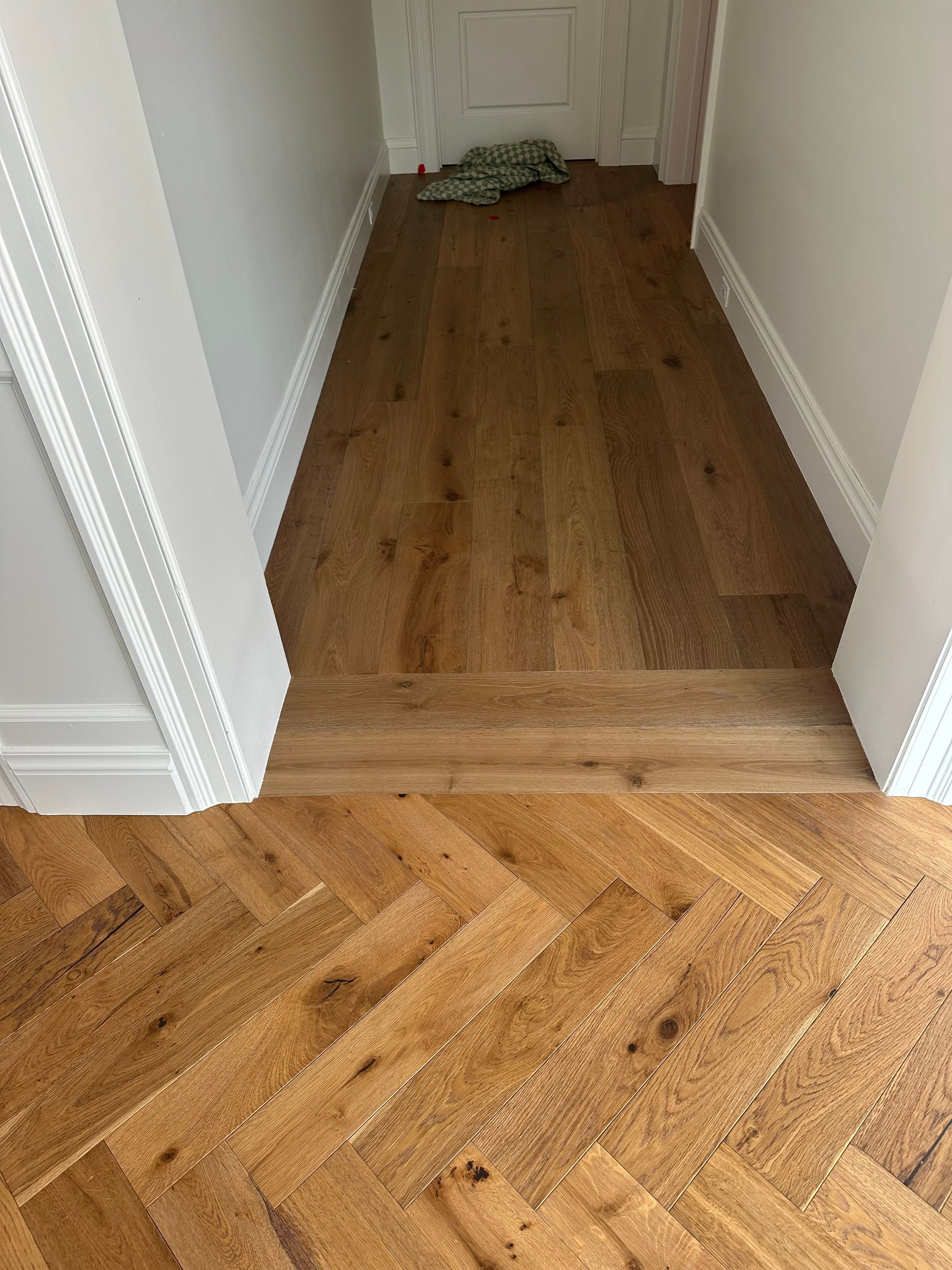 Wooden floors transition from herringbone to planks, with white trim and walls.