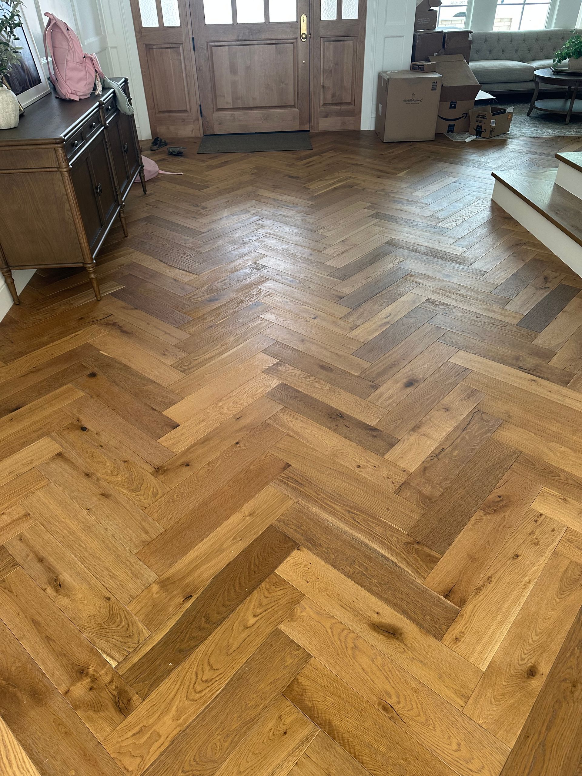 Herringbone pattern hardwood floor in entryway, leading to wooden door, brown tones.