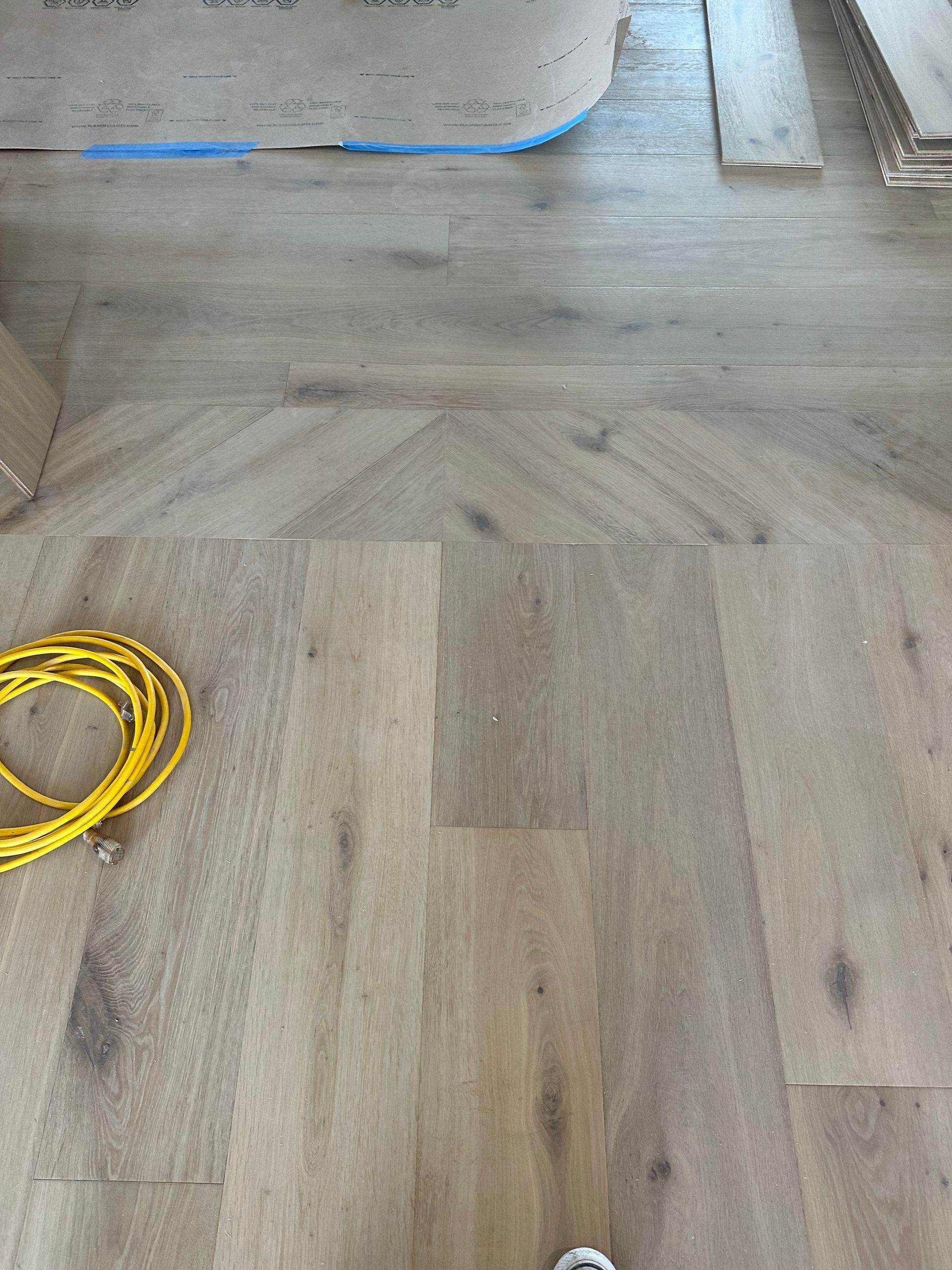 Light wood flooring installation in progress. Yellow wire, blue tape, and wood pieces visible.