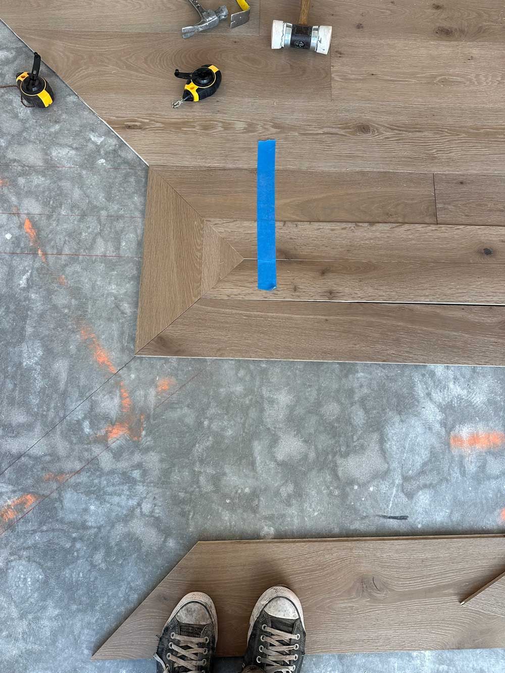 Overhead shot: Feet in sneakers at bottom, blue block in the center, toys and wood on floor.