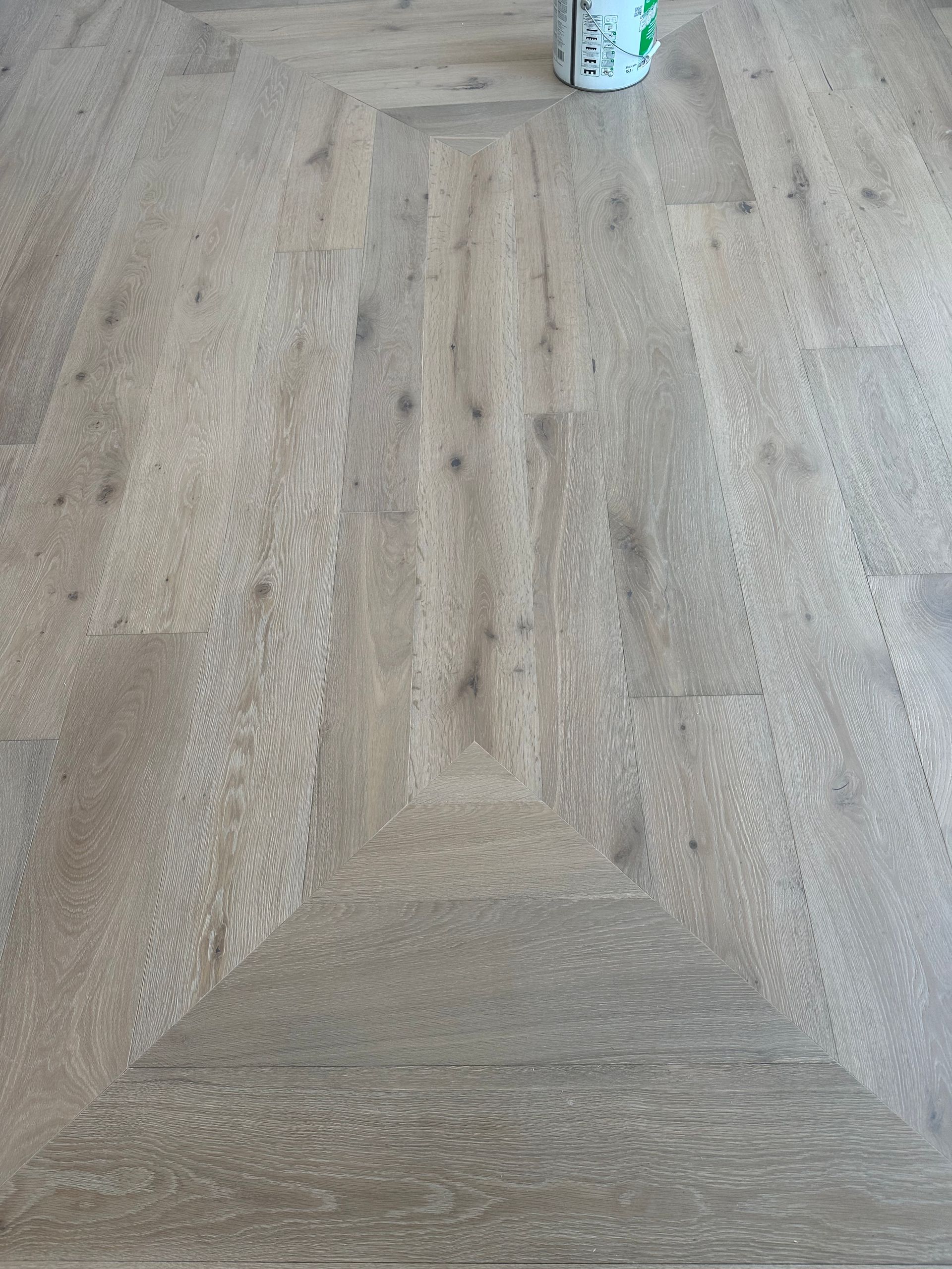 Light wood floor with a central geometric design, with a can on the floor.