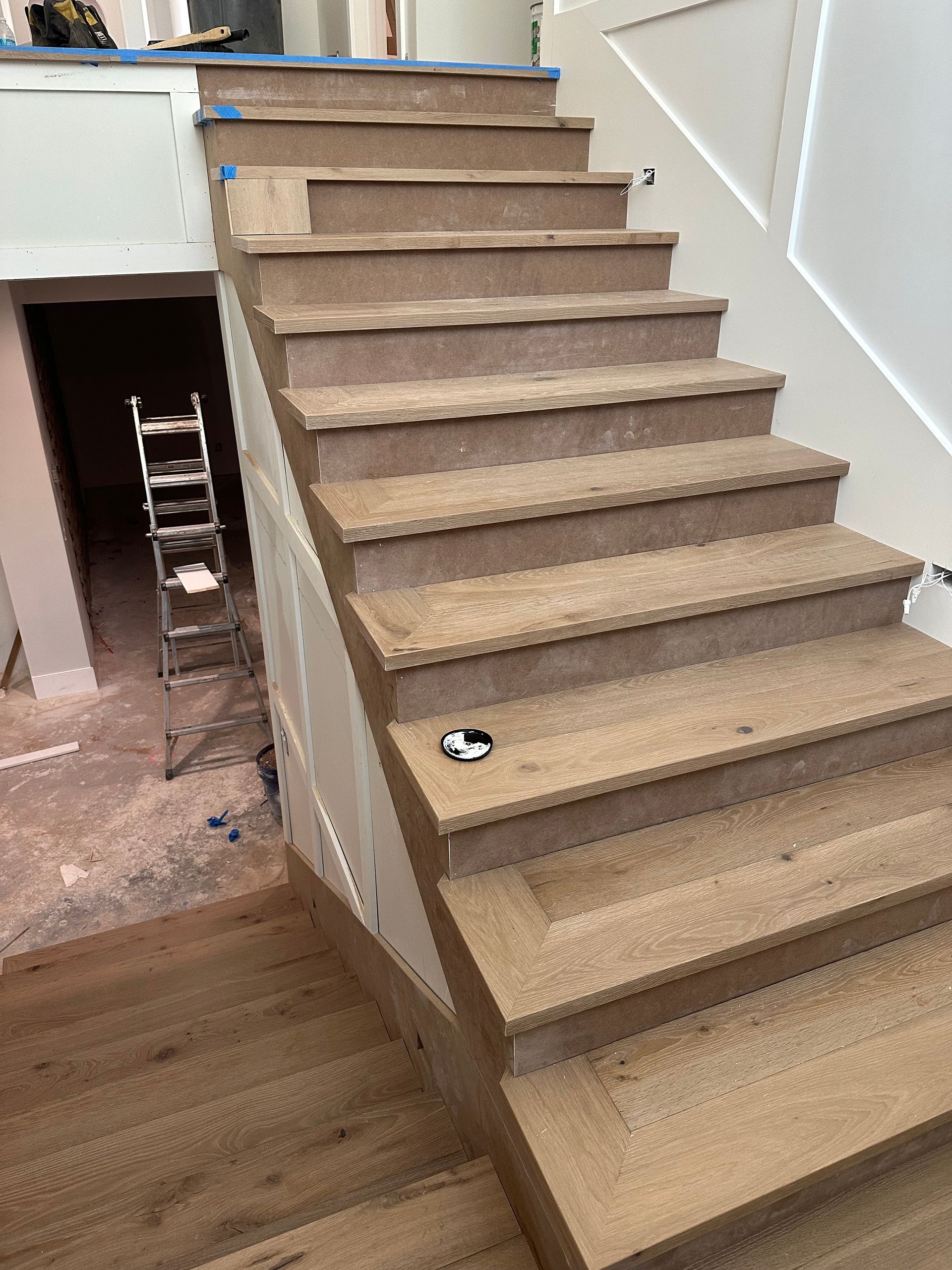 Wooden staircase under construction with a ladder in the background.