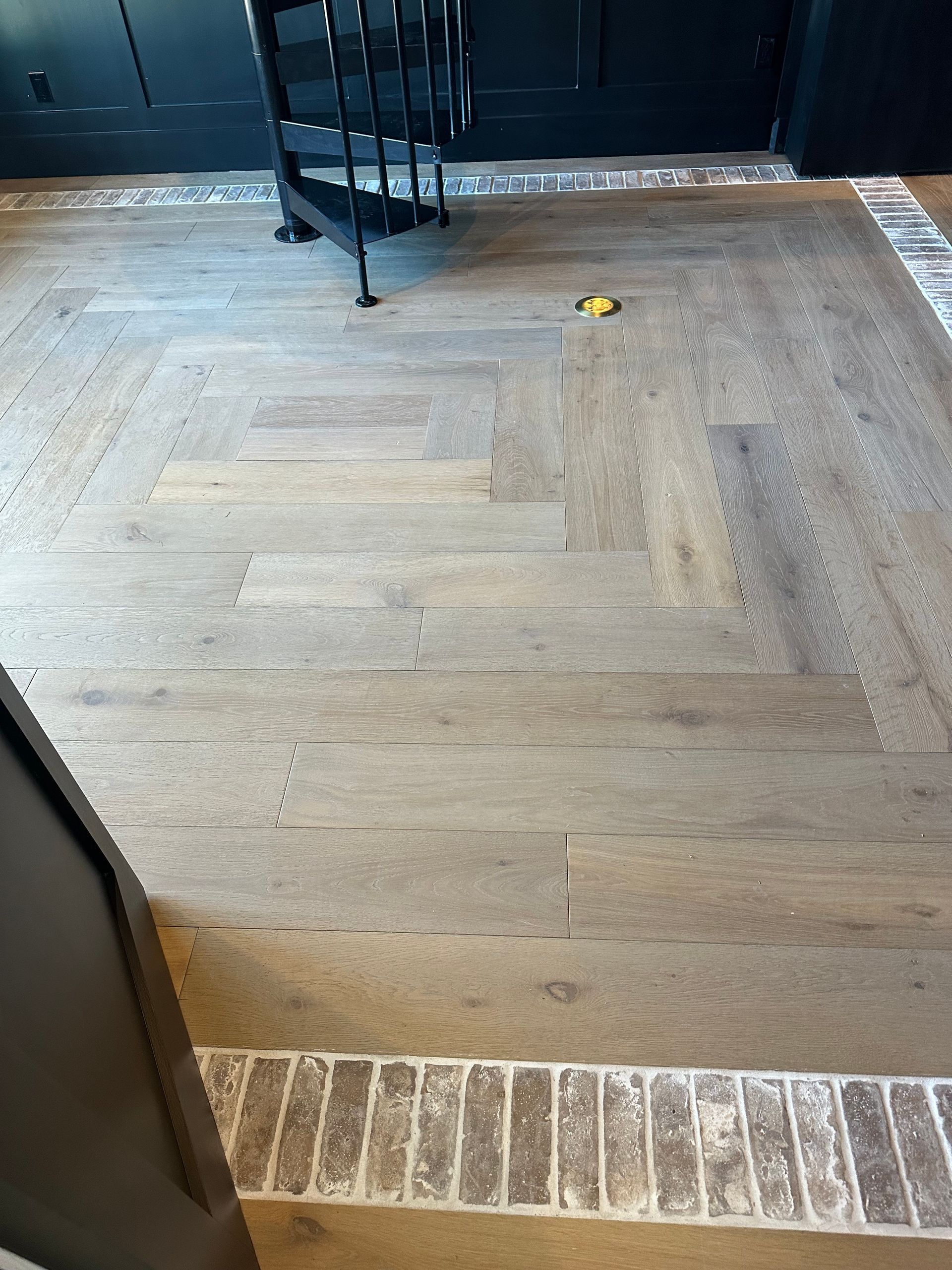 Herringbone wooden floor with a brick border; a chair sits on the floor.