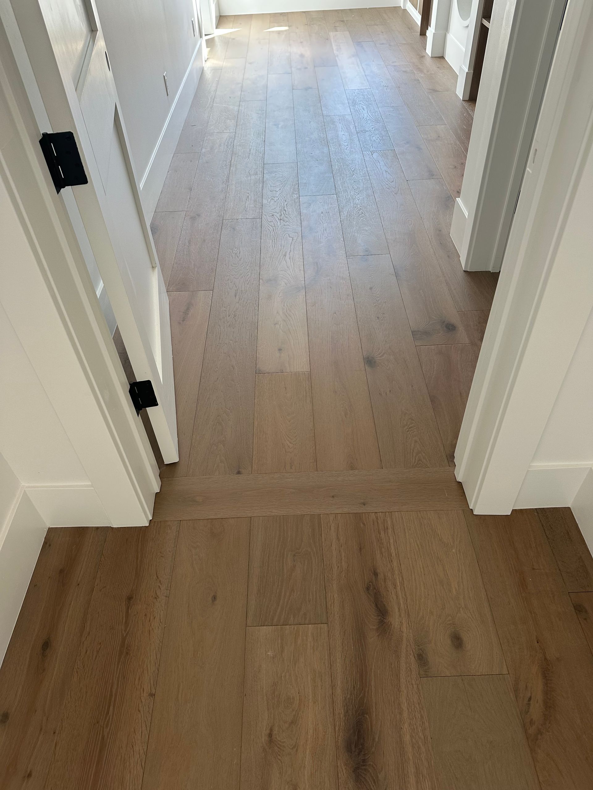 Hardwood flooring in hallway, light brown with wood grain. White doors and trim.