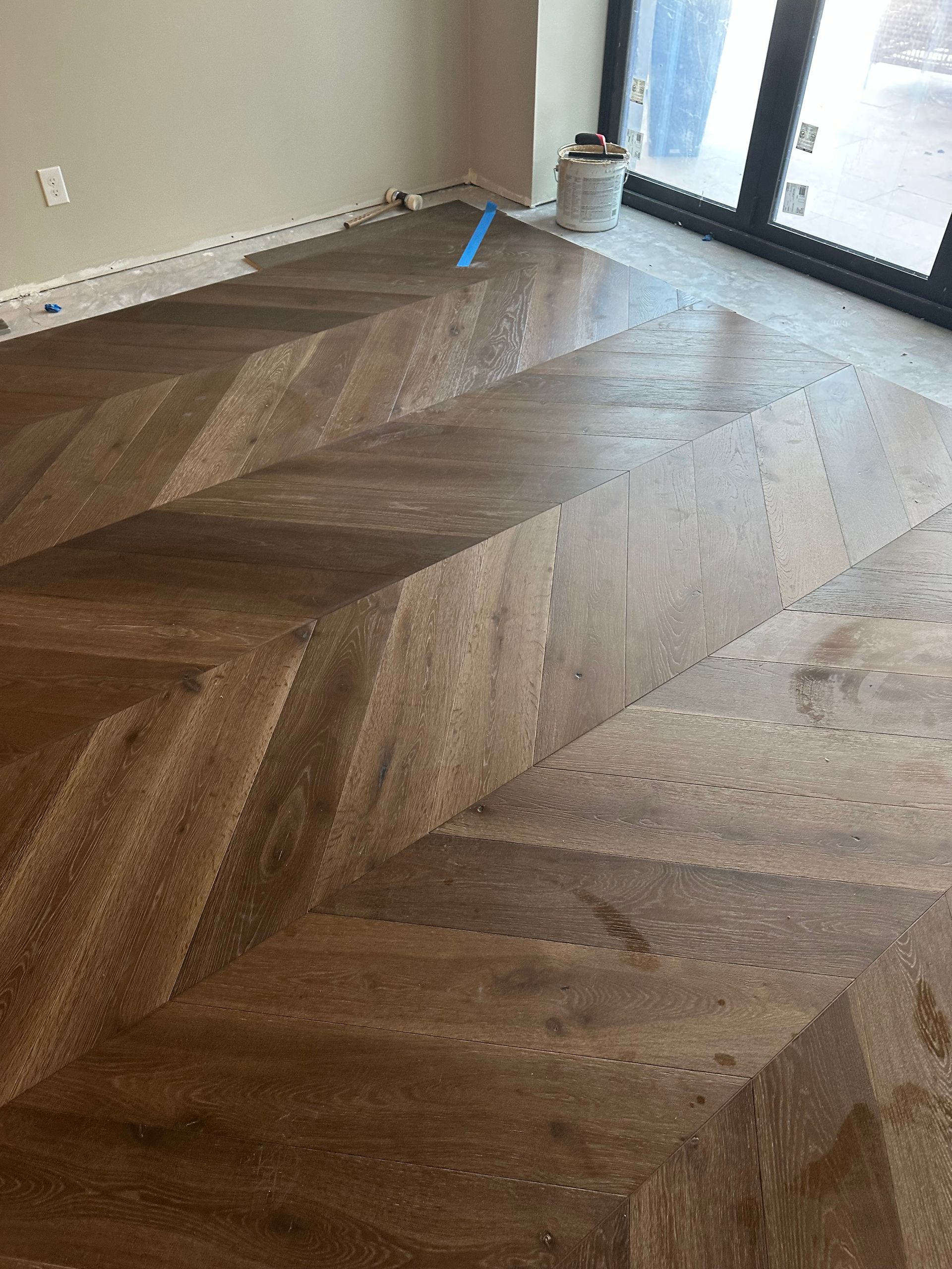 Herringbone pattern wood floor with tan and brown tones, partially finished.