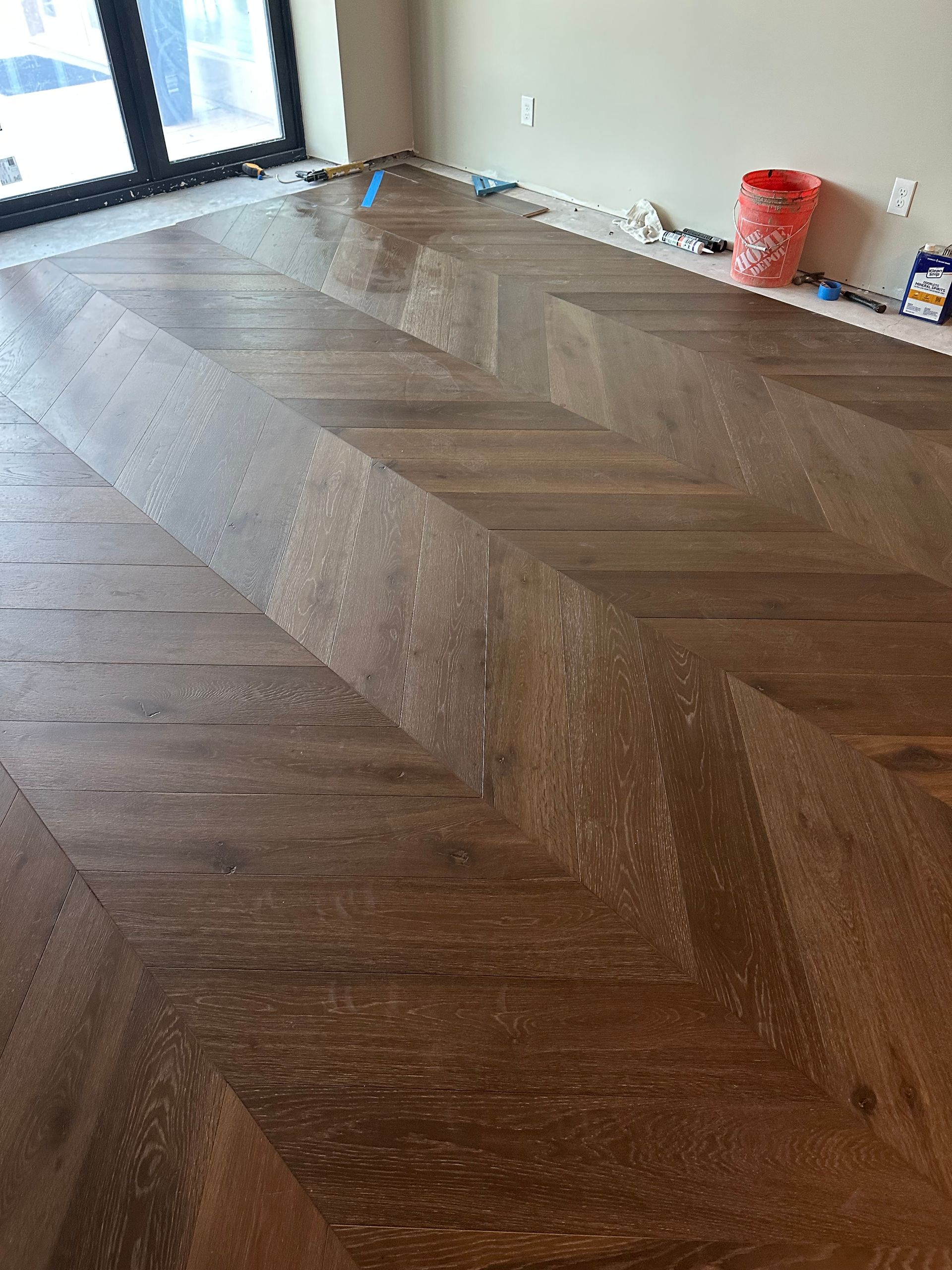 Herringbone pattern hardwood floor in a room with a window.