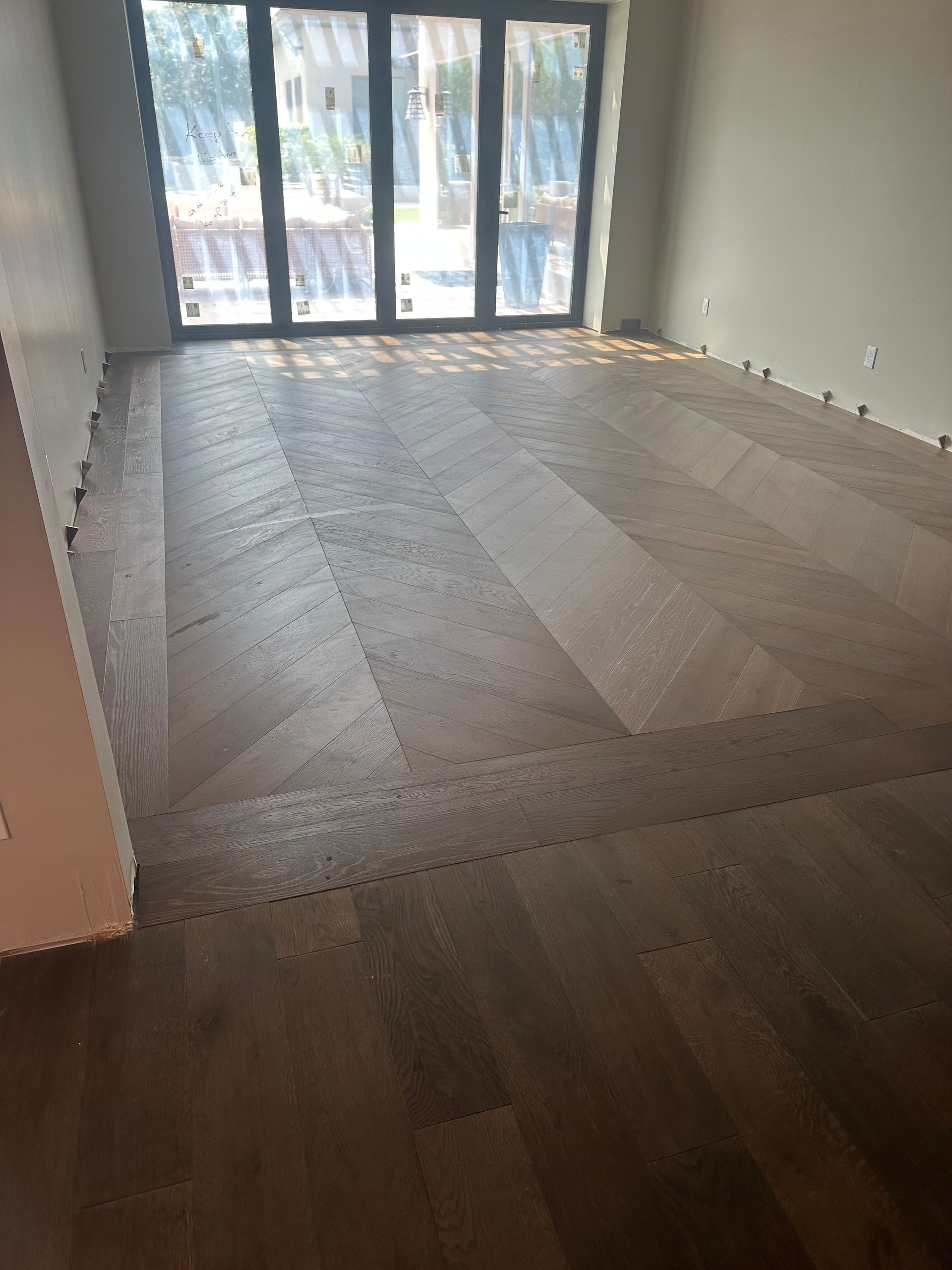 Dark wood floor being installed in a room, with a glass door visible in the background.