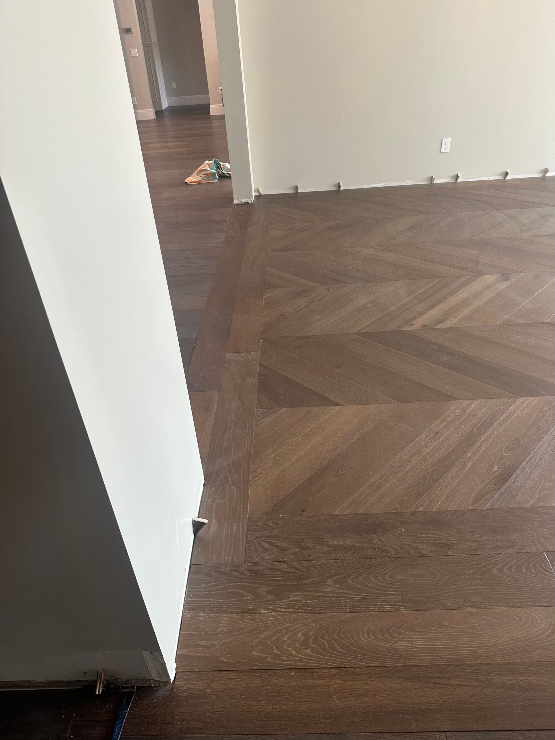 Dark wood floor with herringbone pattern next to a white wall.