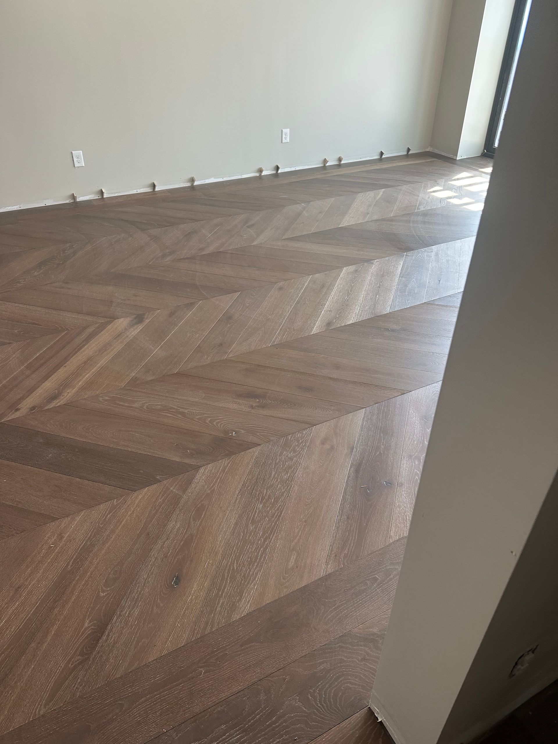 Herringbone pattern wood floor with brown tones in an empty room.