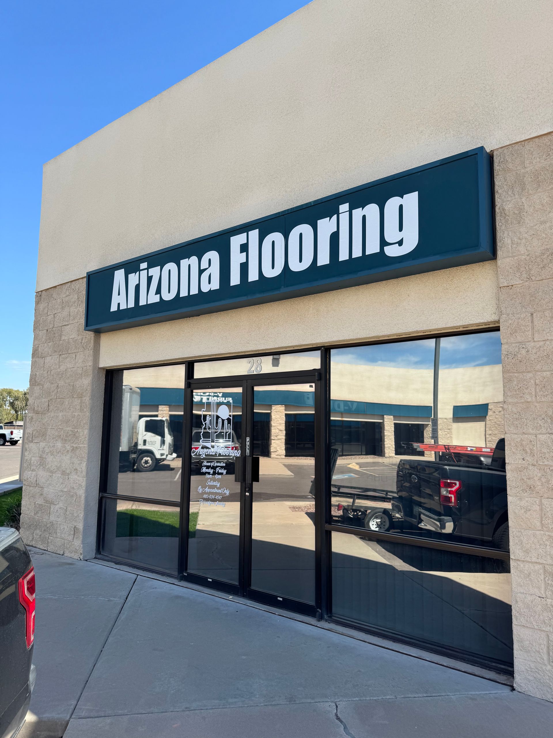 Arizona Flooring store with glass doors, a blue sign, and a truck reflected in the windows.