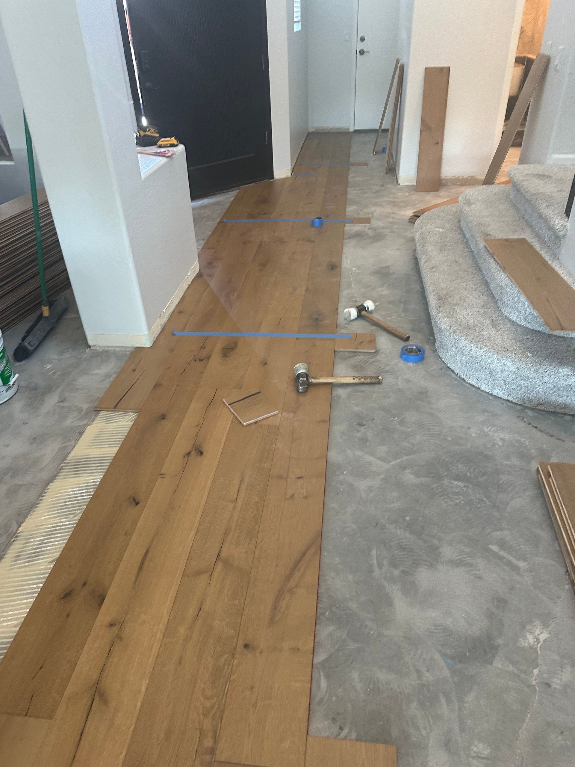 Wooden floorboards being installed on a concrete subfloor; tools and materials visible.
