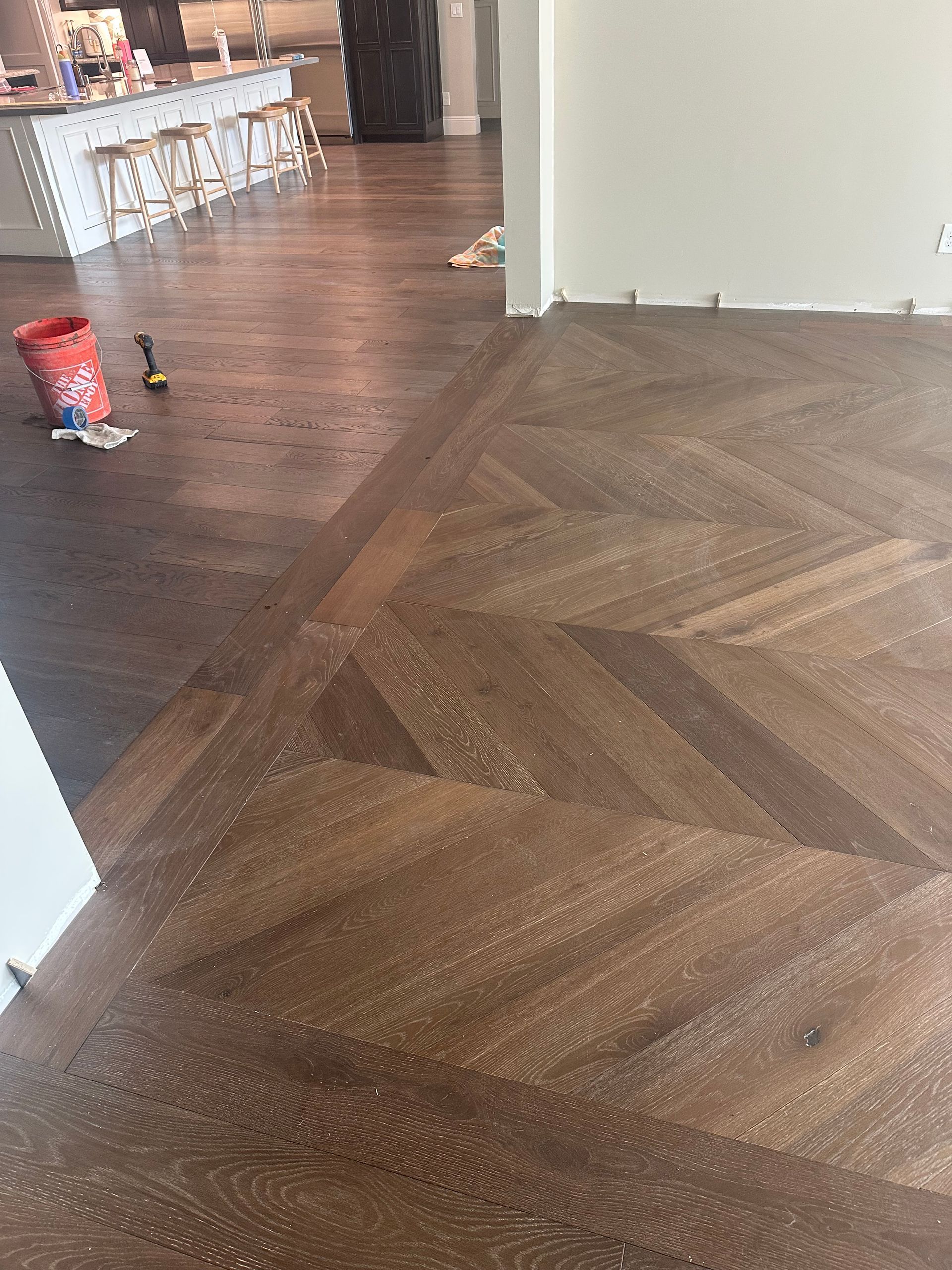 Herringbone pattern hardwood floor, dark stain. Open kitchen area visible, construction in progress.