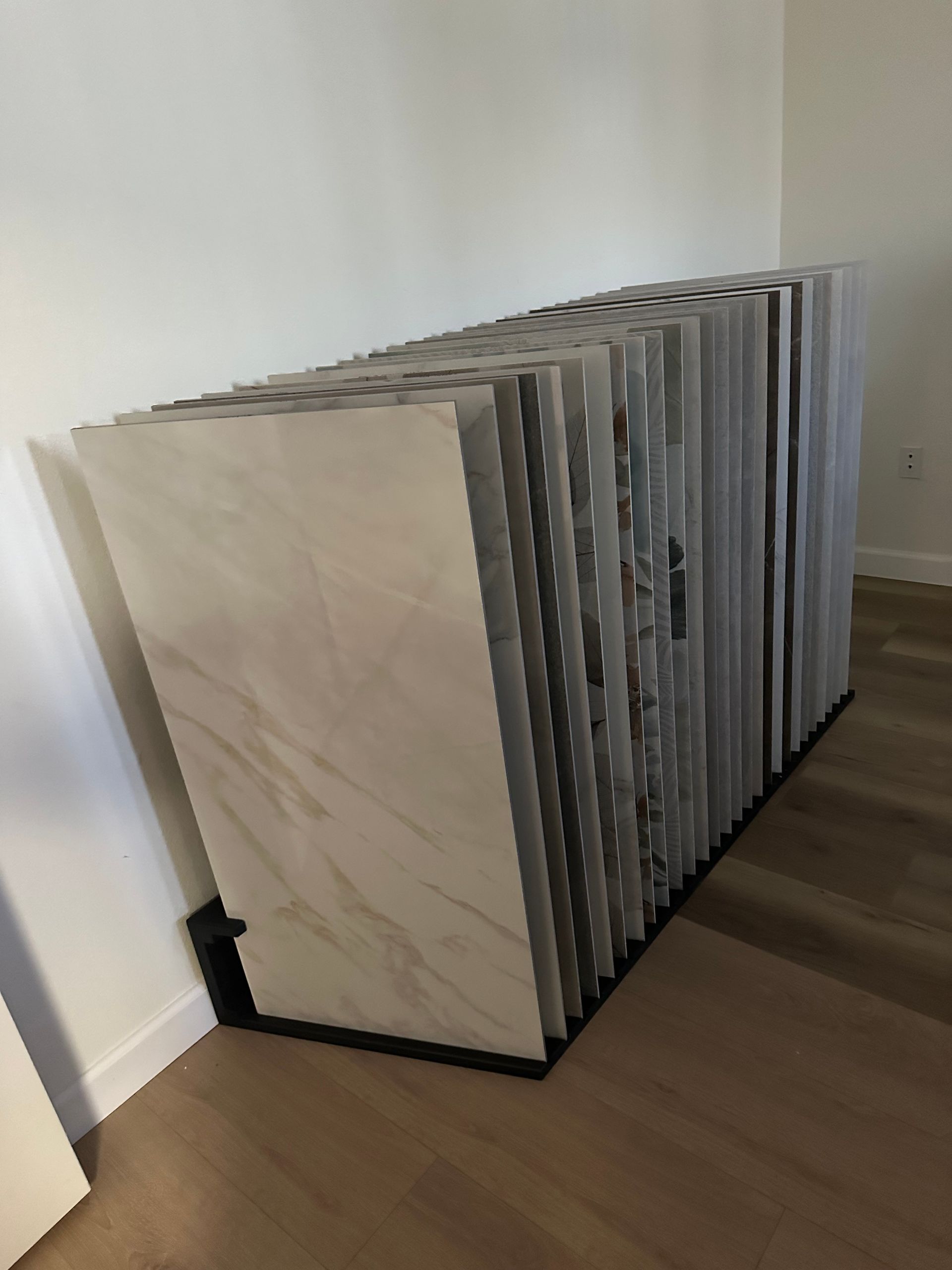 Tile samples displayed in a rack, leaning against a white wall on a wood floor.