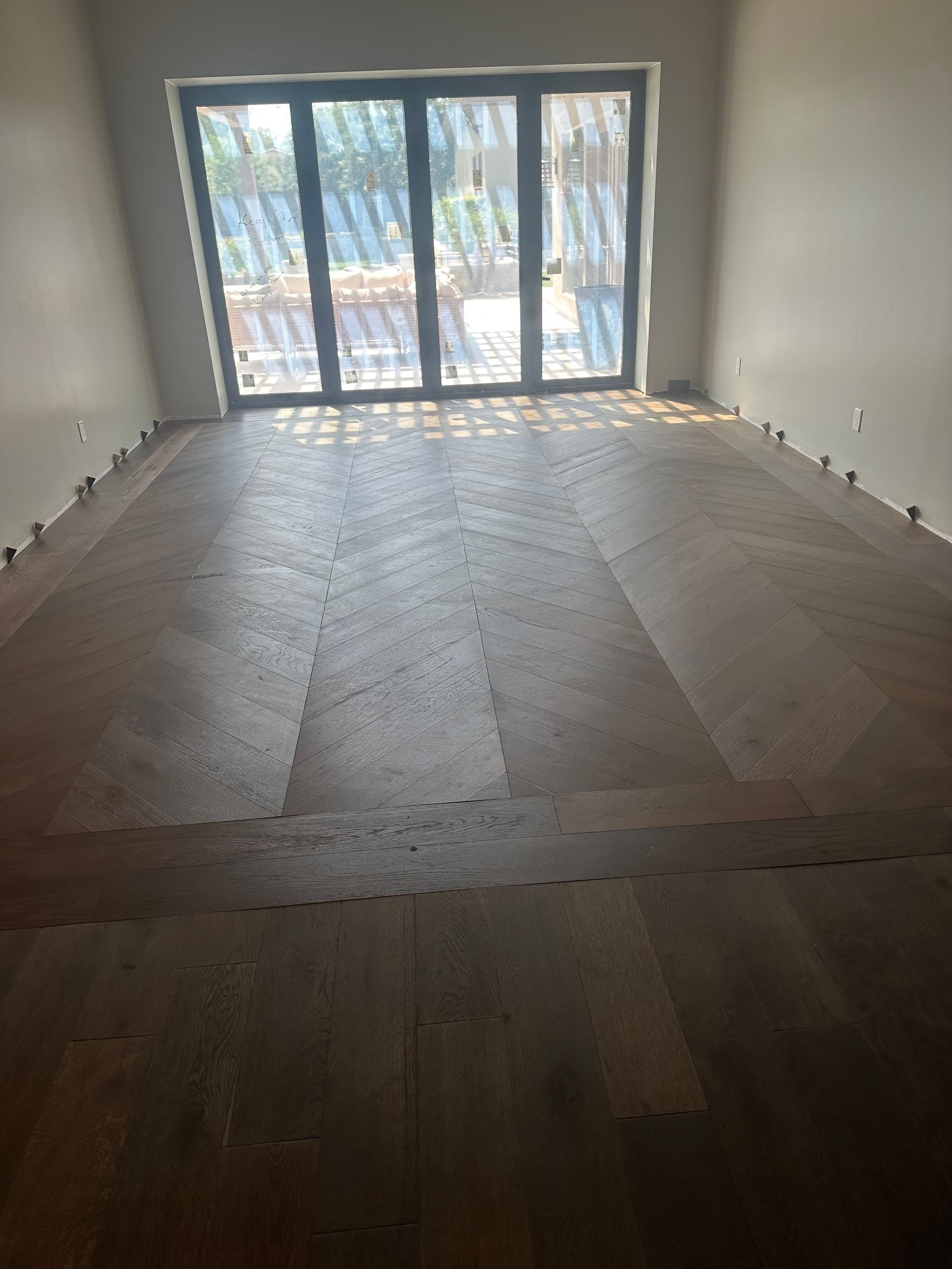 A room with newly installed wooden flooring and a large window.