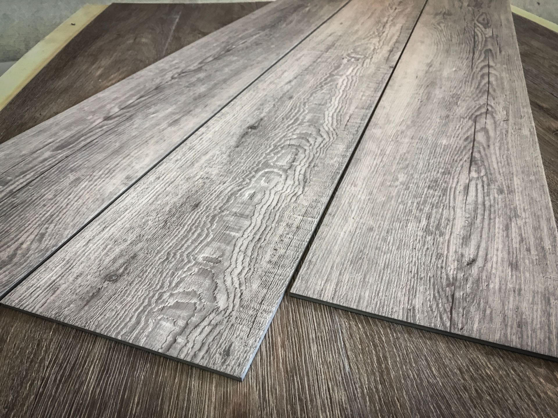 Three gray wood-look flooring planks, arranged on a darker wood surface.