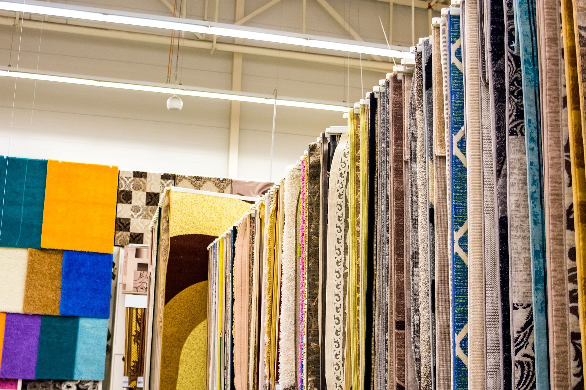 Rugs of various patterns and colors hanging in a store.