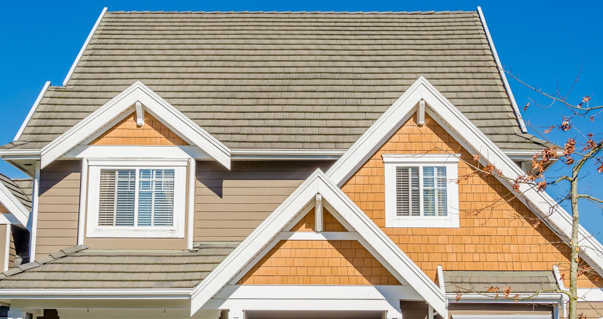 Tan and orange house with white trim and a brown roof against a clear blue sky.