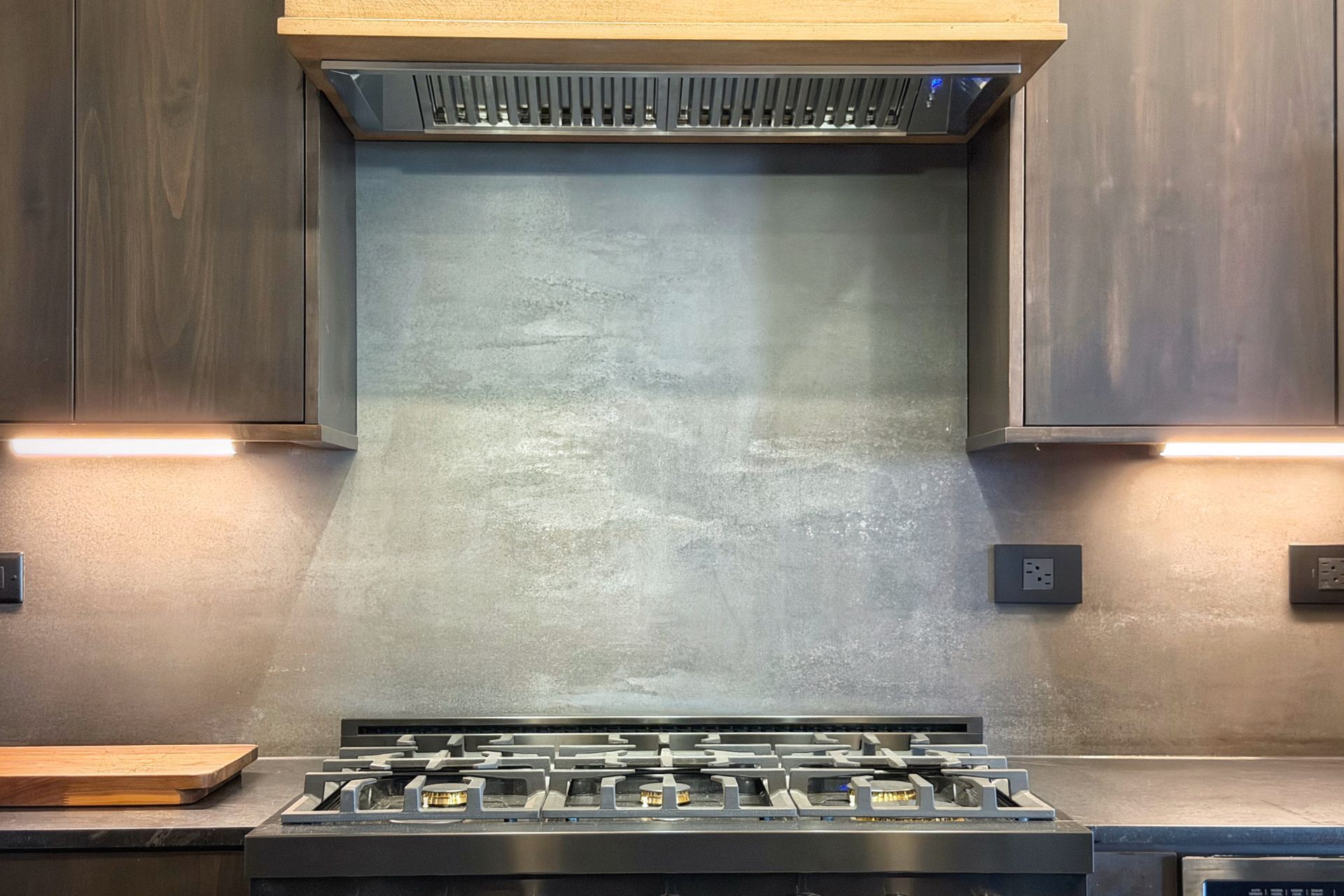 Modern kitchen with gas cooktop, stainless hood, and gray textured backsplash
