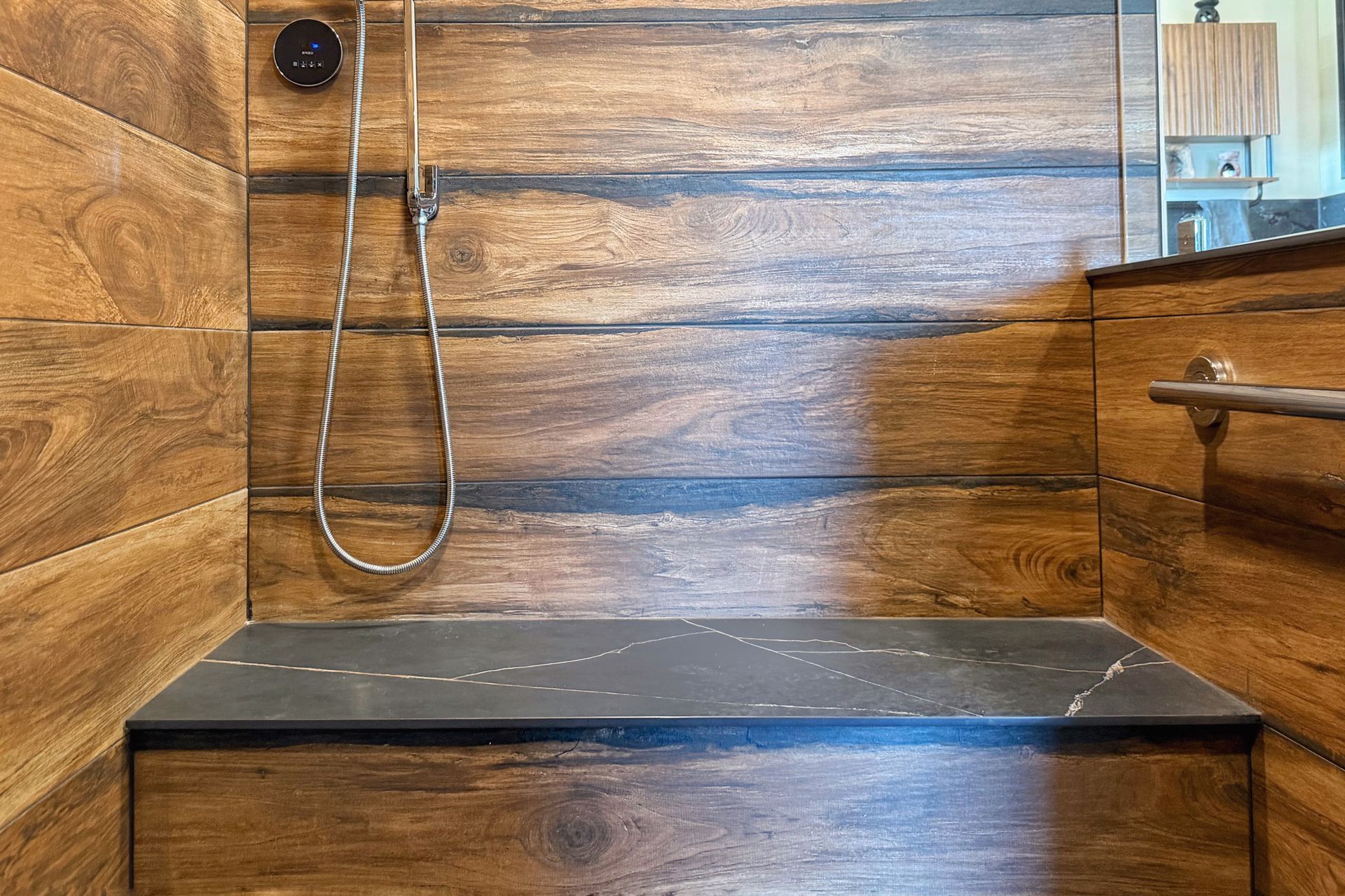 Wood-paneled shower with black bench, handheld showerhead, and chrome grab bar