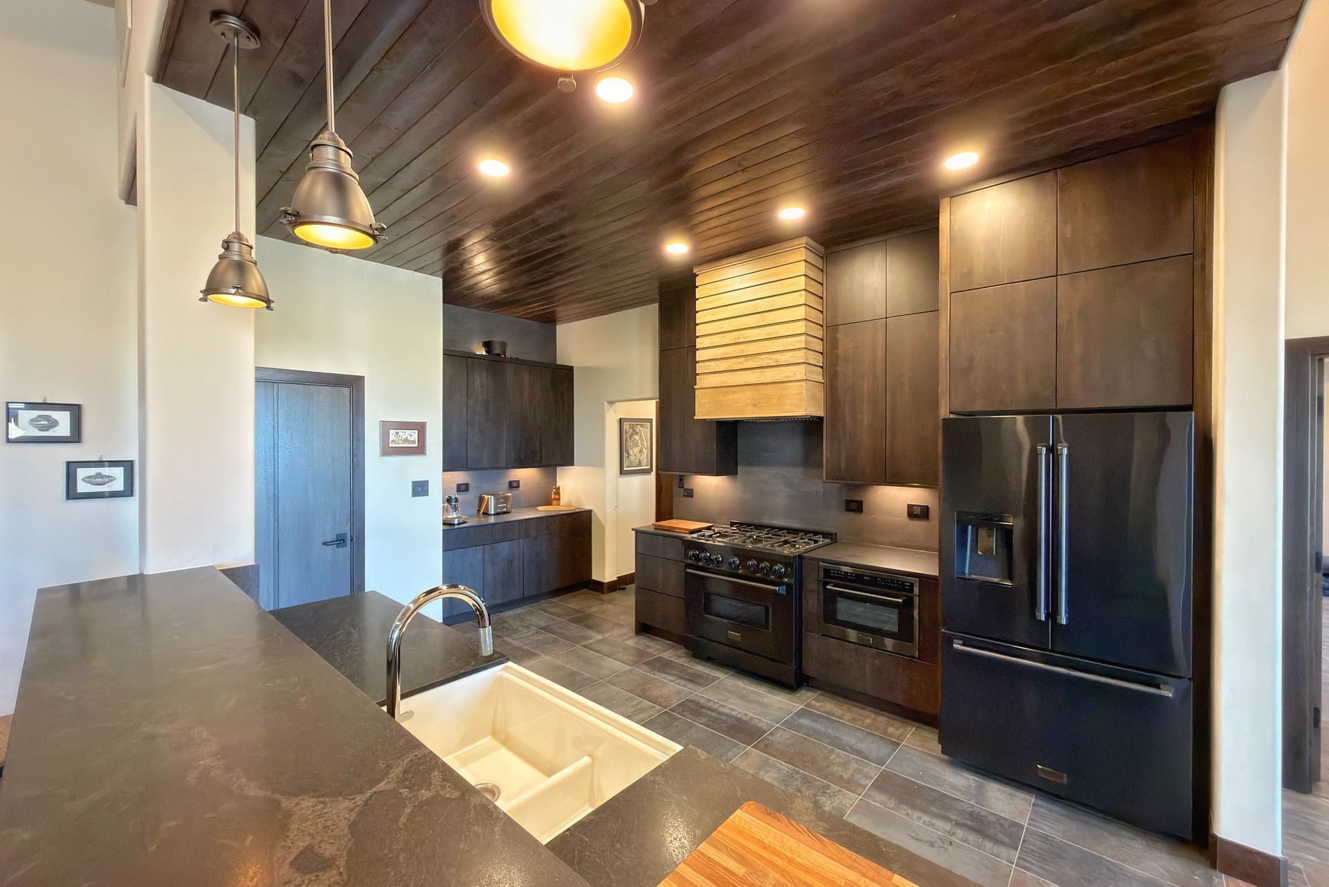 Modern kitchen with dark wood cabinets, black appliances, and pendant lights over a granite island