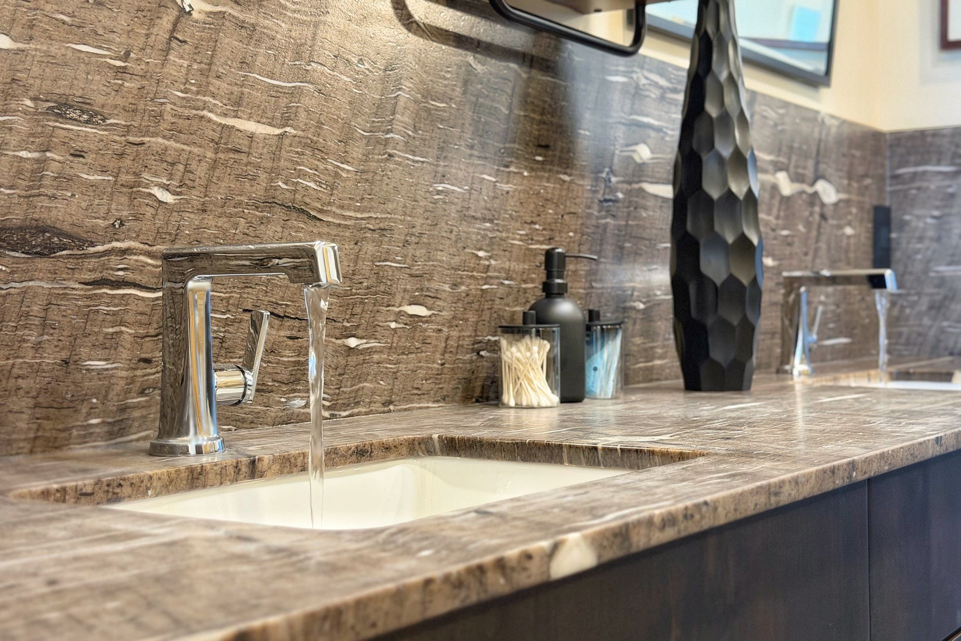 Modern bathroom vanity with double sinks, chrome faucets, stone backsplash, and black decor centerpiece