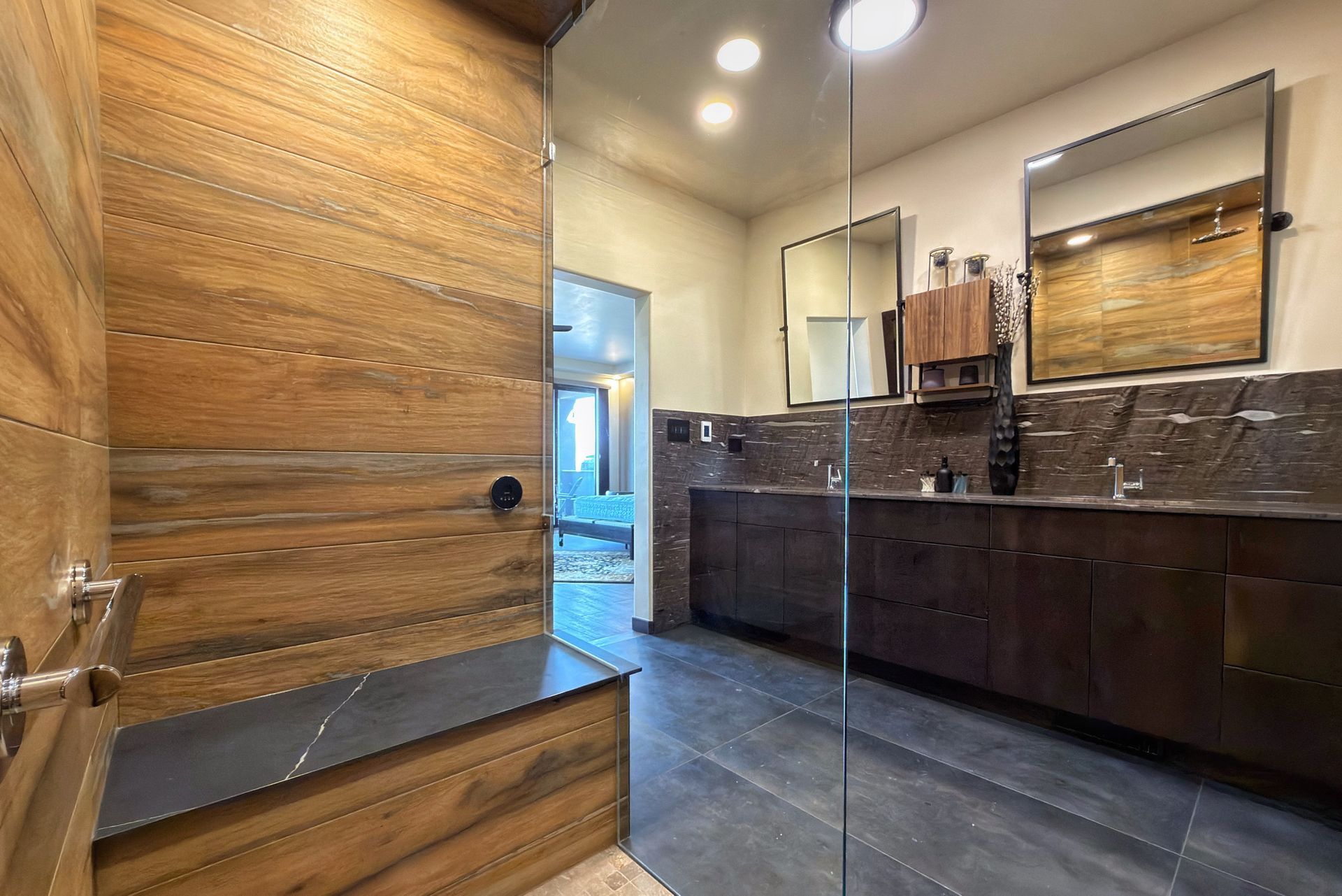 Modern bathroom with dark wood vanity, large mirror, stone countertops, and a walk-in shower.