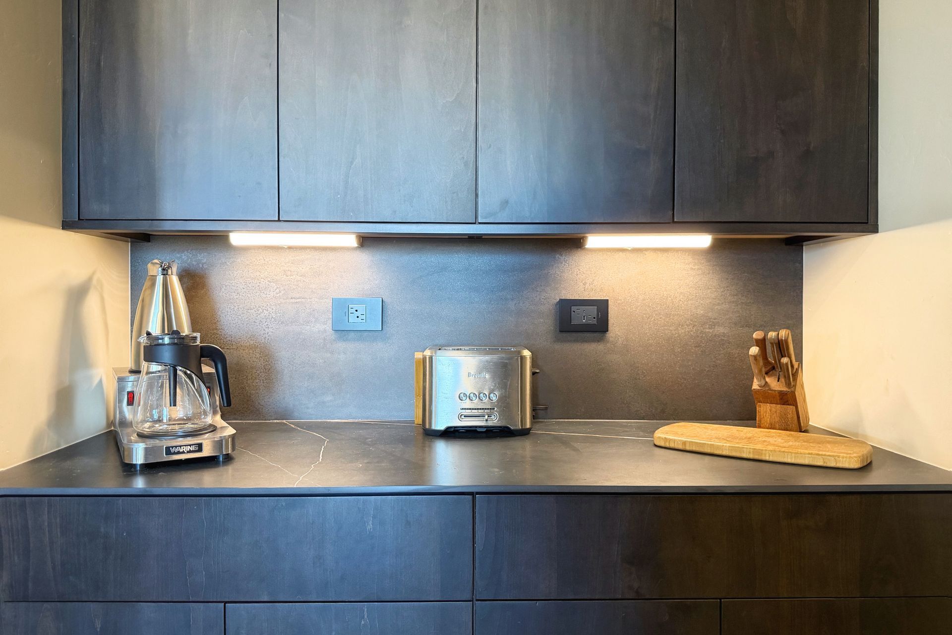 Modern kitchen counter with toaster, coffee maker, utensil holder, and under-cabinet lighting