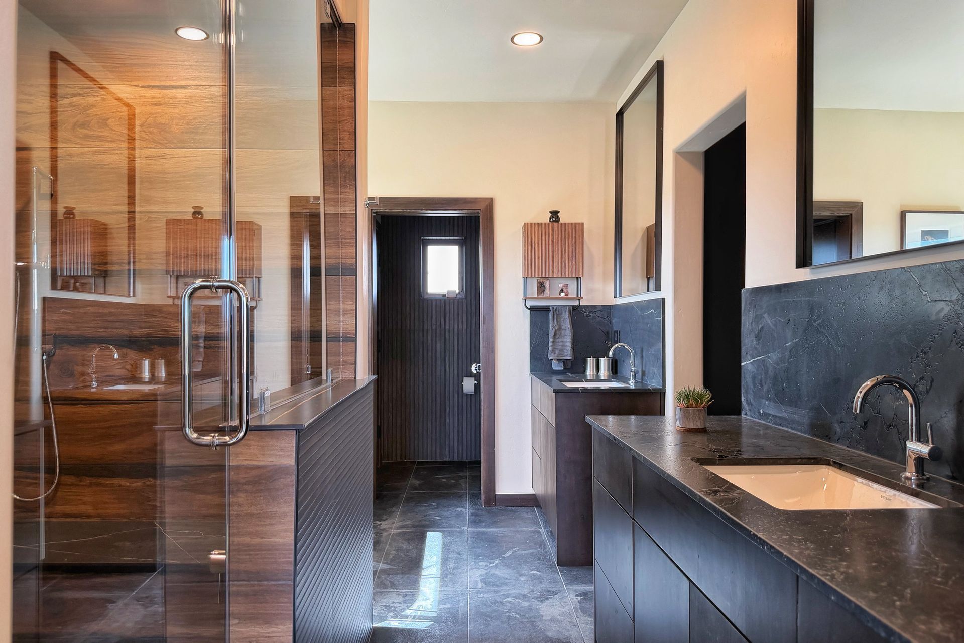 Modern bathroom with glass shower, dark vanity, and black tile finishes