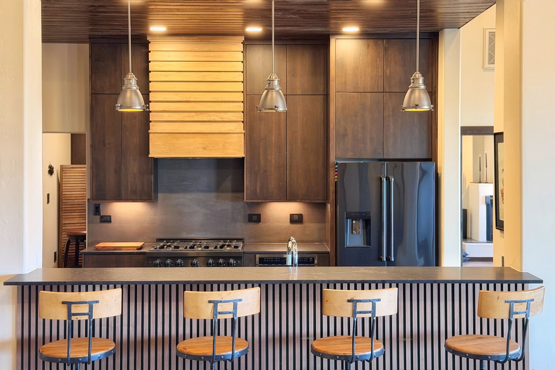 Modern kitchen with dark wood cabinets, pendant lights, island seating, and a stainless steel refrigerator