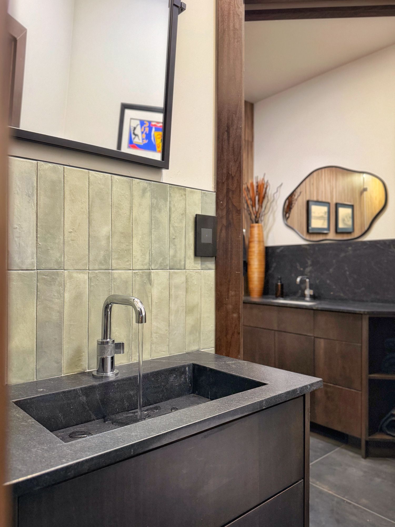 Modern bathroom with black sink vanity, chrome faucet, tile wall, and round mirror over a dark wood cabinet.