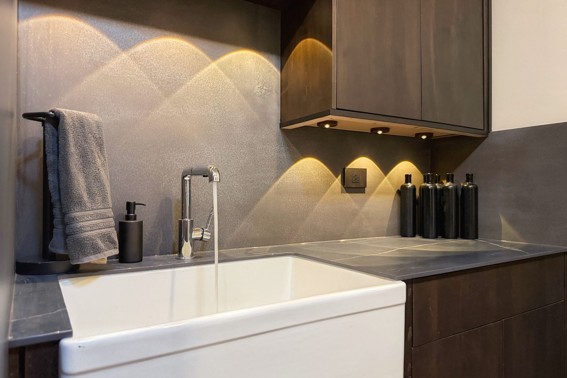 Modern kitchen sink area with white apron sink, dark wood cabinets, and warm under-cabinet lighting