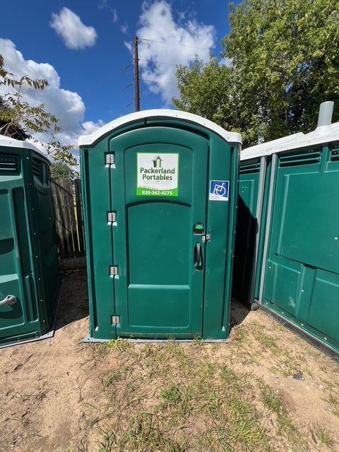 Man in grey jacket cleans the door of a purple portable toilet with a white cloth, outdoors.
