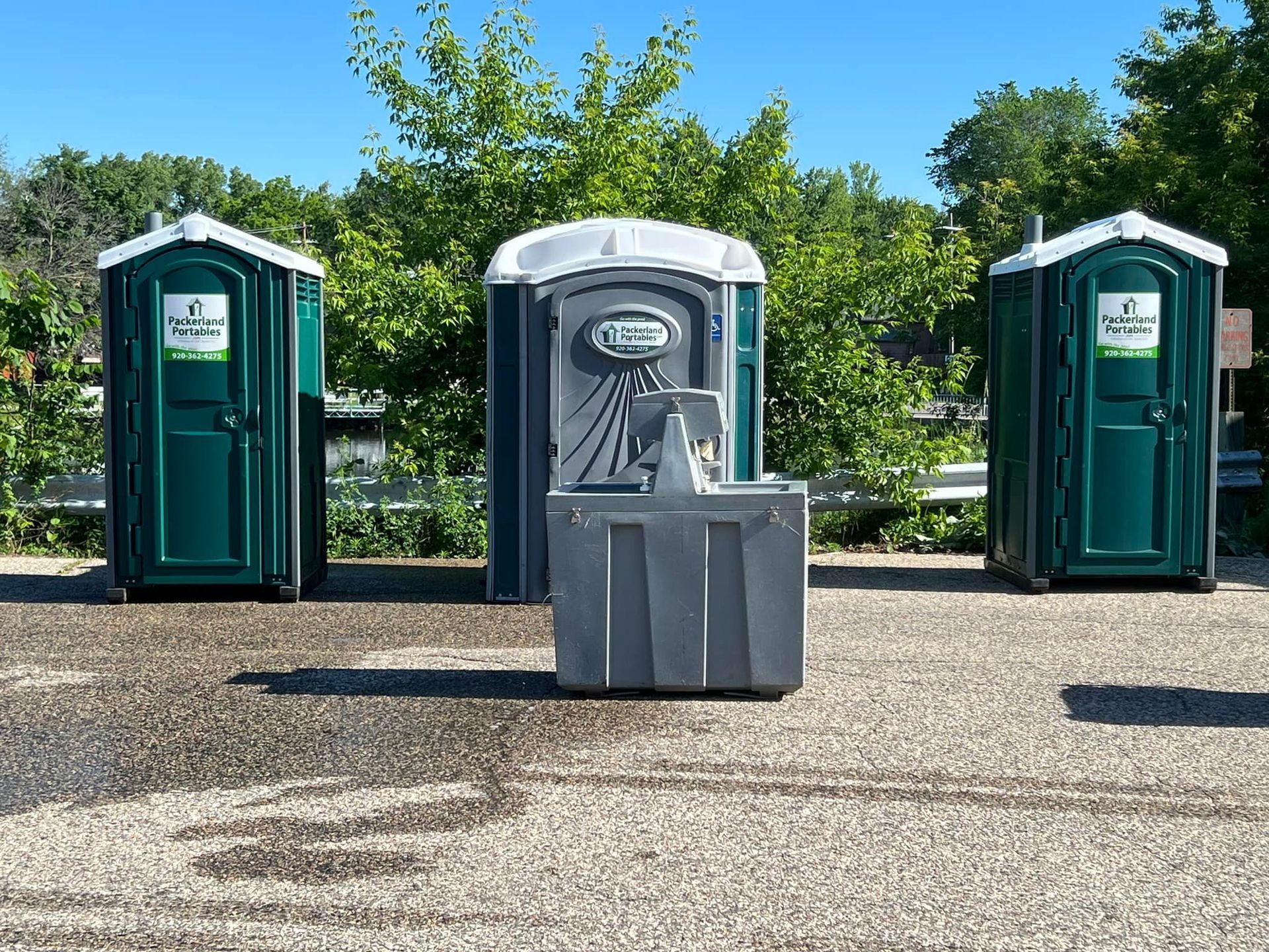 Row of portable toilets of various colors in front of a brick building.