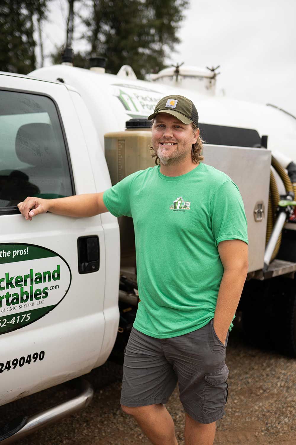 Man in green shirt and hat leans against a white truck with company logo.