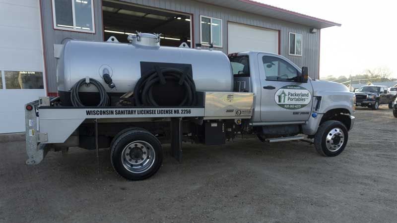 Silver septic tank truck parked outside a garage.