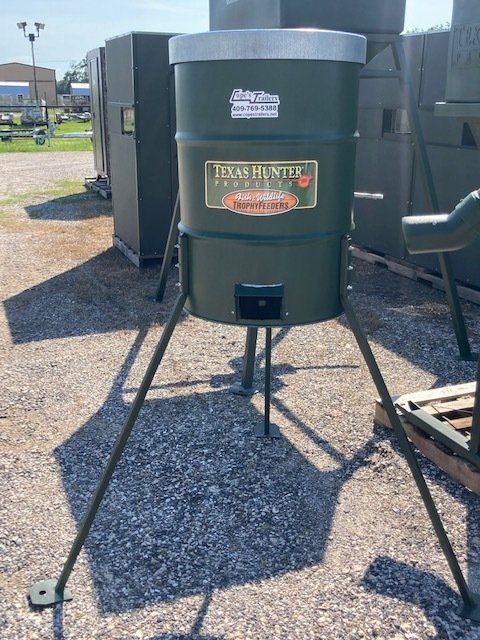 A green feeder is sitting on top of a gravel road.