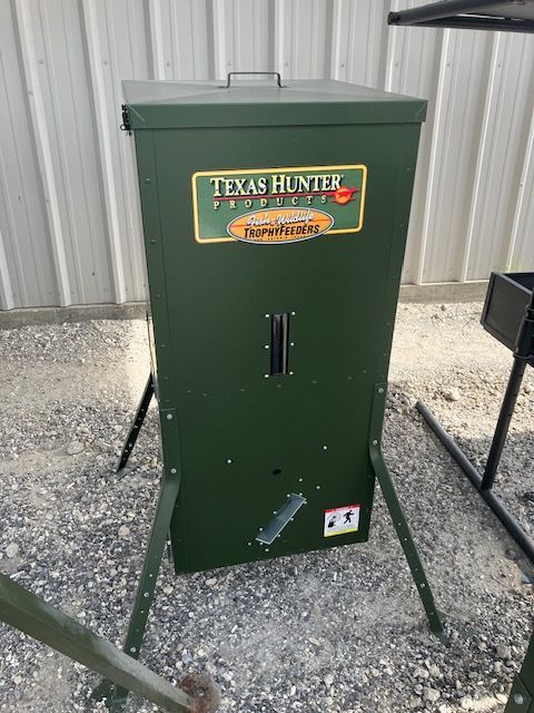 A green texas hunter feeder is sitting on the ground in front of a building.