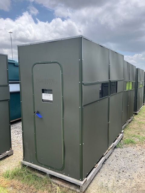 A row of green buildings are sitting on top of a gravel lot.